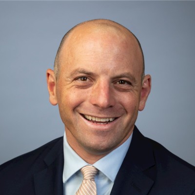 A person in a suit smilingDescription automatically generated