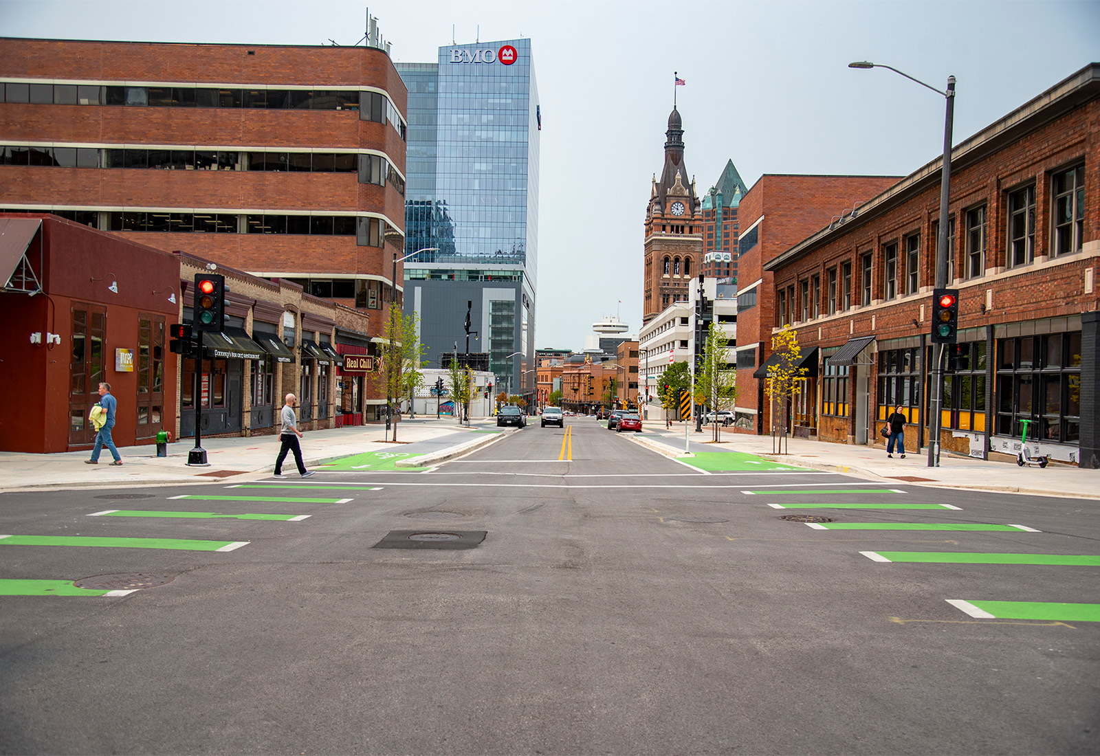View looking east along East Wells Street in downtown Milwaukee, showing protected bike lanes, green bike crossings, pedestrian crosswalks, and streetscape improvements designed to support safe travel for people walking, biking, and driving.