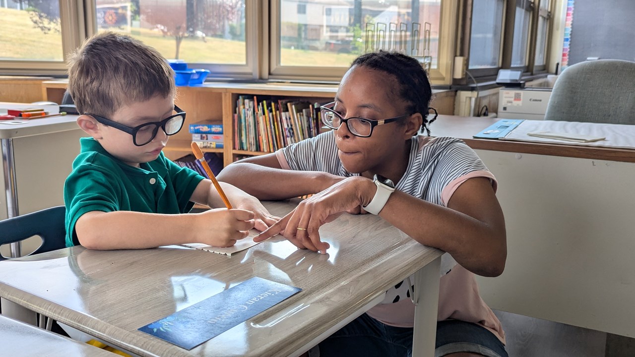 Center School teacher supporting young 1st grade student with his work. 