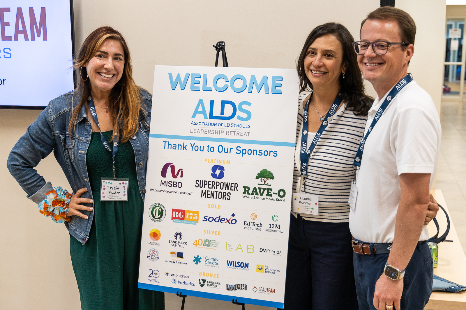 3 conference leaders gathered around a retreat poster sign, smiling