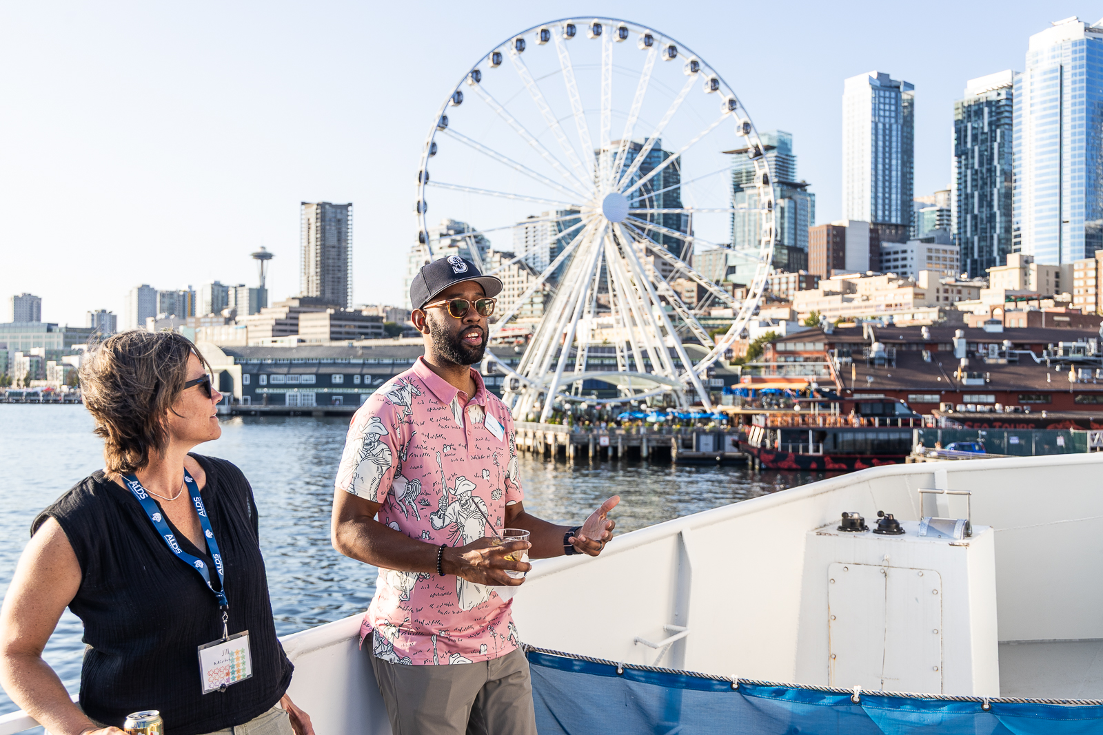 One attendee speaking on a boat with beautiful ferris wheel in the background, with another attendee smiling and looking on