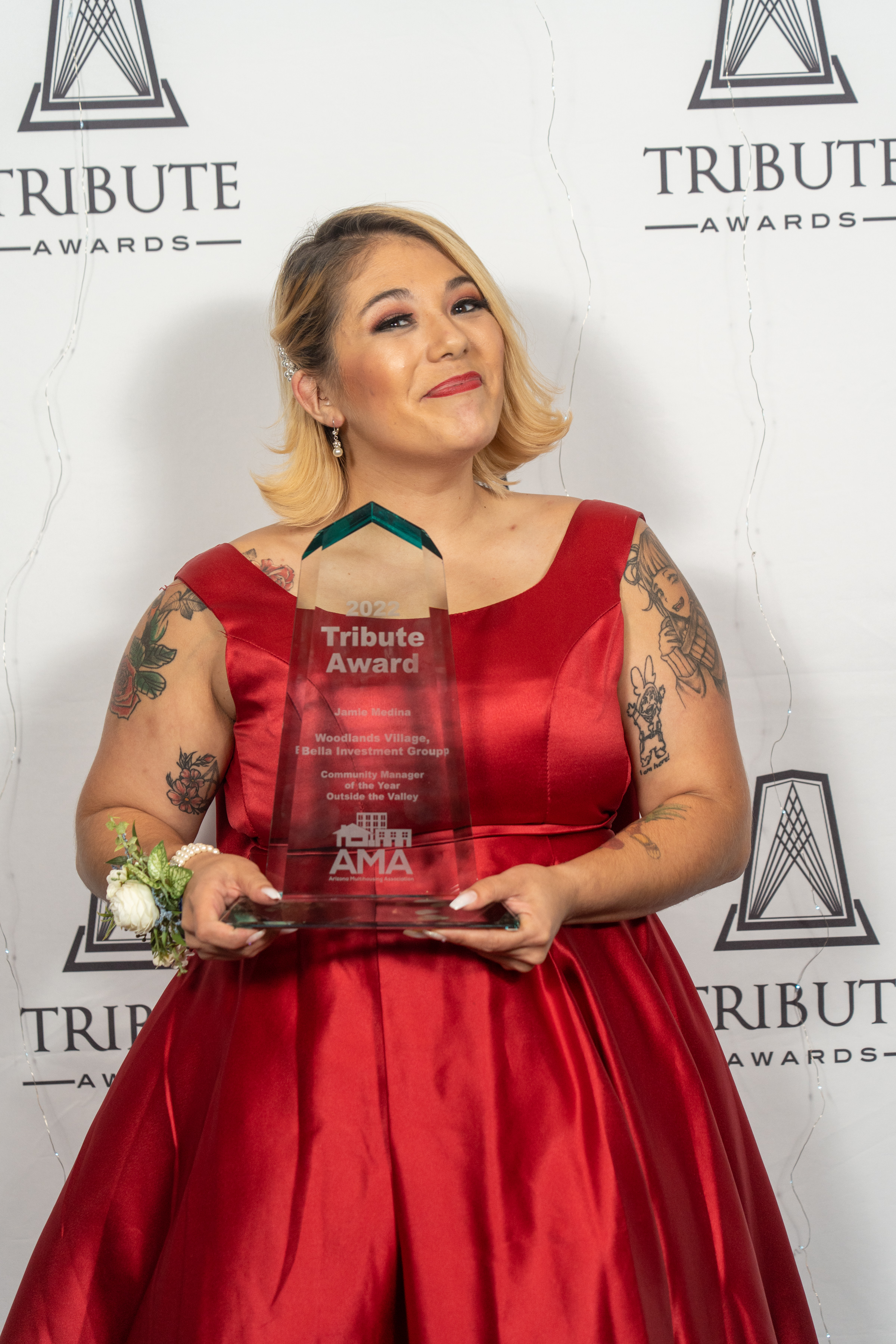 A woman in a red gown holding an award at the tribute awards event.