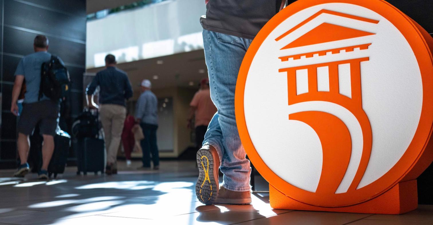 An orange APPA logo sign in a hotel lobby as attendees arrive for APPAU St. Louis