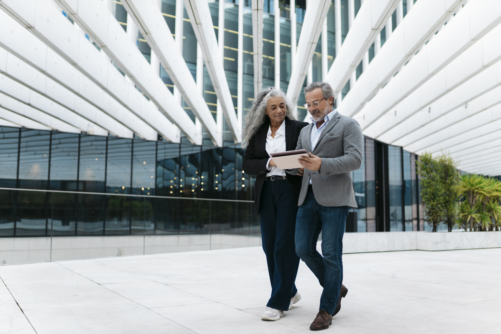 Two senior facilities leaders walking and reviewing notes on a tablet outside a campus building
