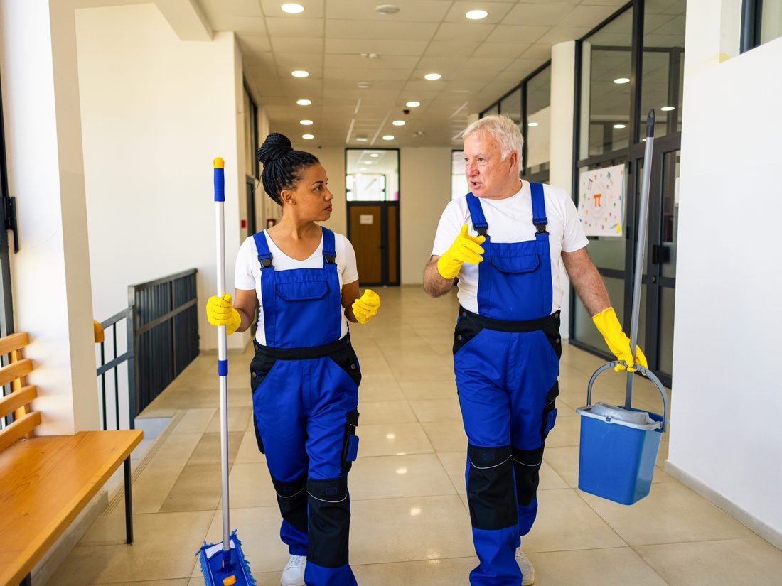 Two custodians talking while working in a school corridor