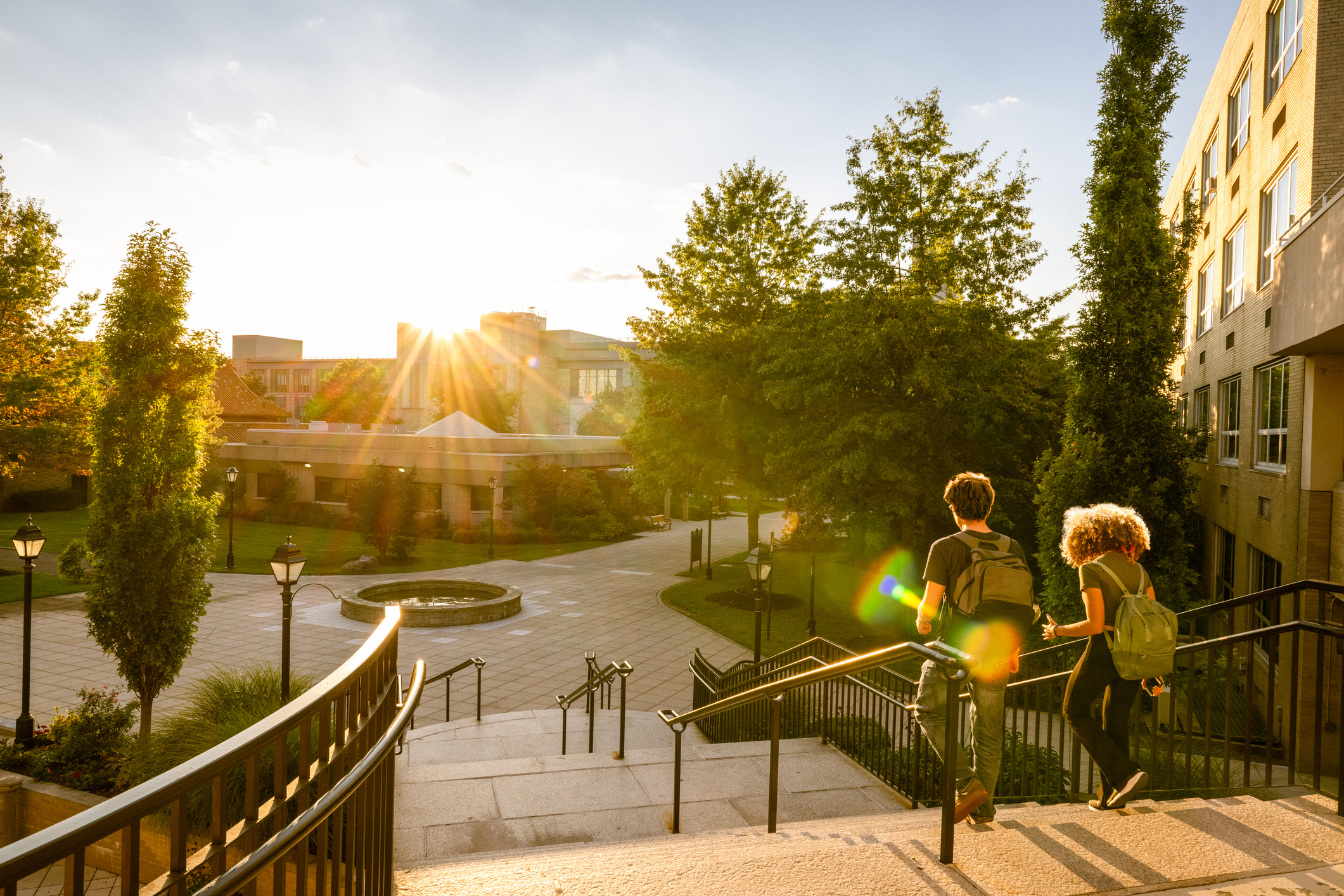 Students walking down campus steps toward a courtyard at sunset