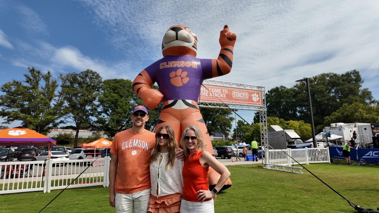 ApartmentsForClemson intern with her parents in front of the Welcome to the Stacks sign and a giant inflatable tiger during Clemson Family Weekend