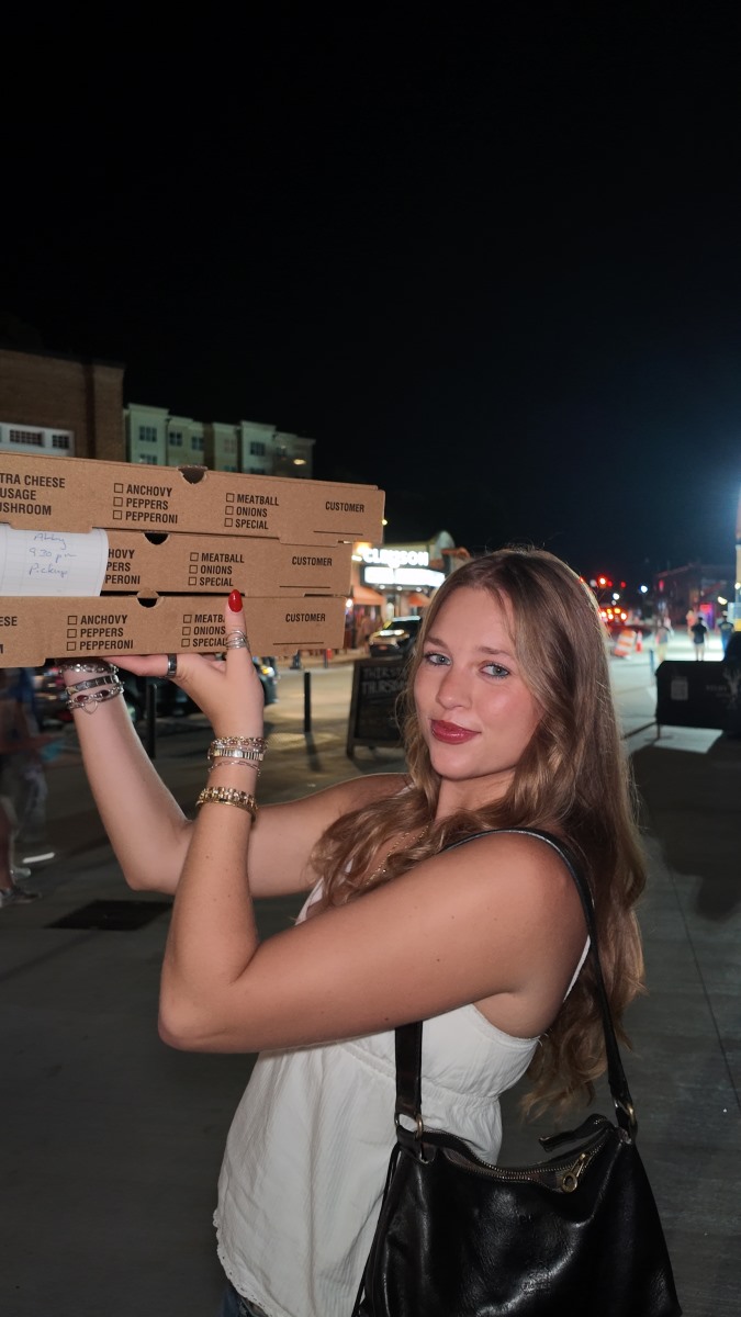 ApartmentsForClemson intern holding a stack of pizza boxes at night in downtown Clemson during Clemson Family Weekend