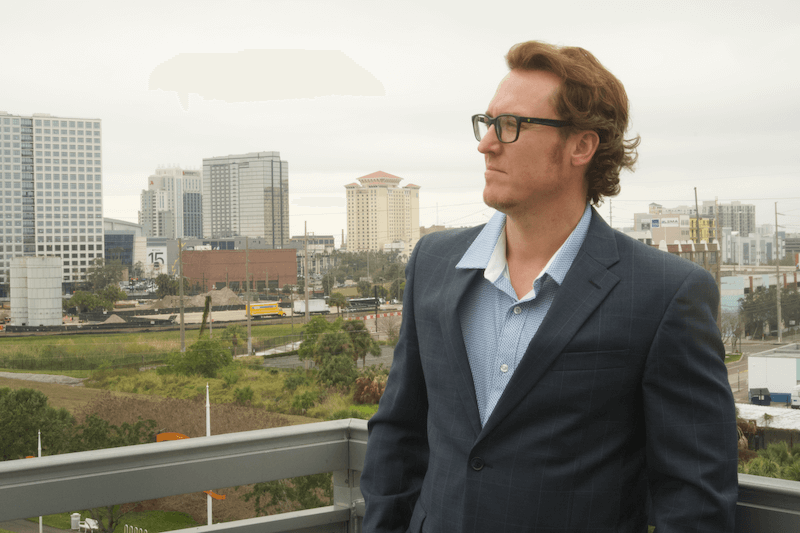 A person in a suit standing on a balcony with a city in the backgroundAI-generated content may be incorrect.