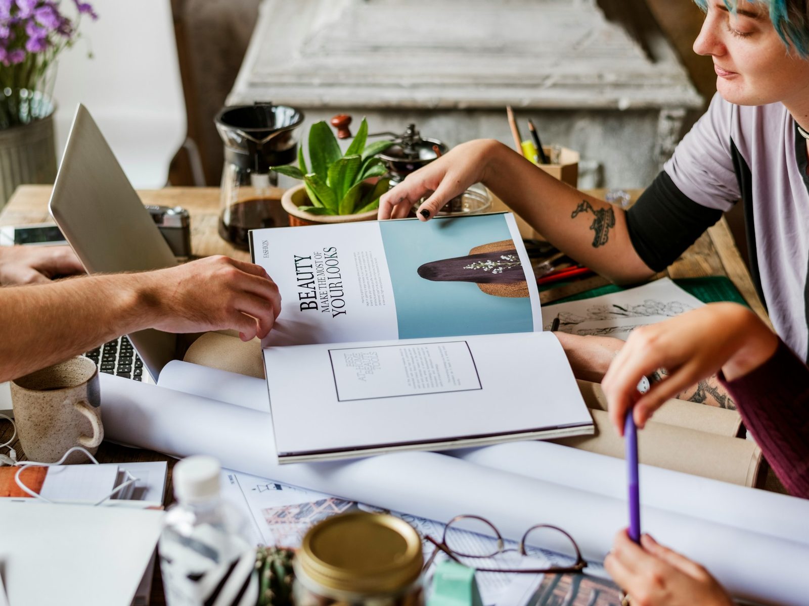 Two people page through an open magazine on a work table