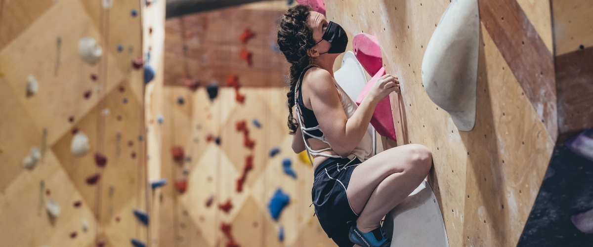 Female rock climber indoors wearing mask 