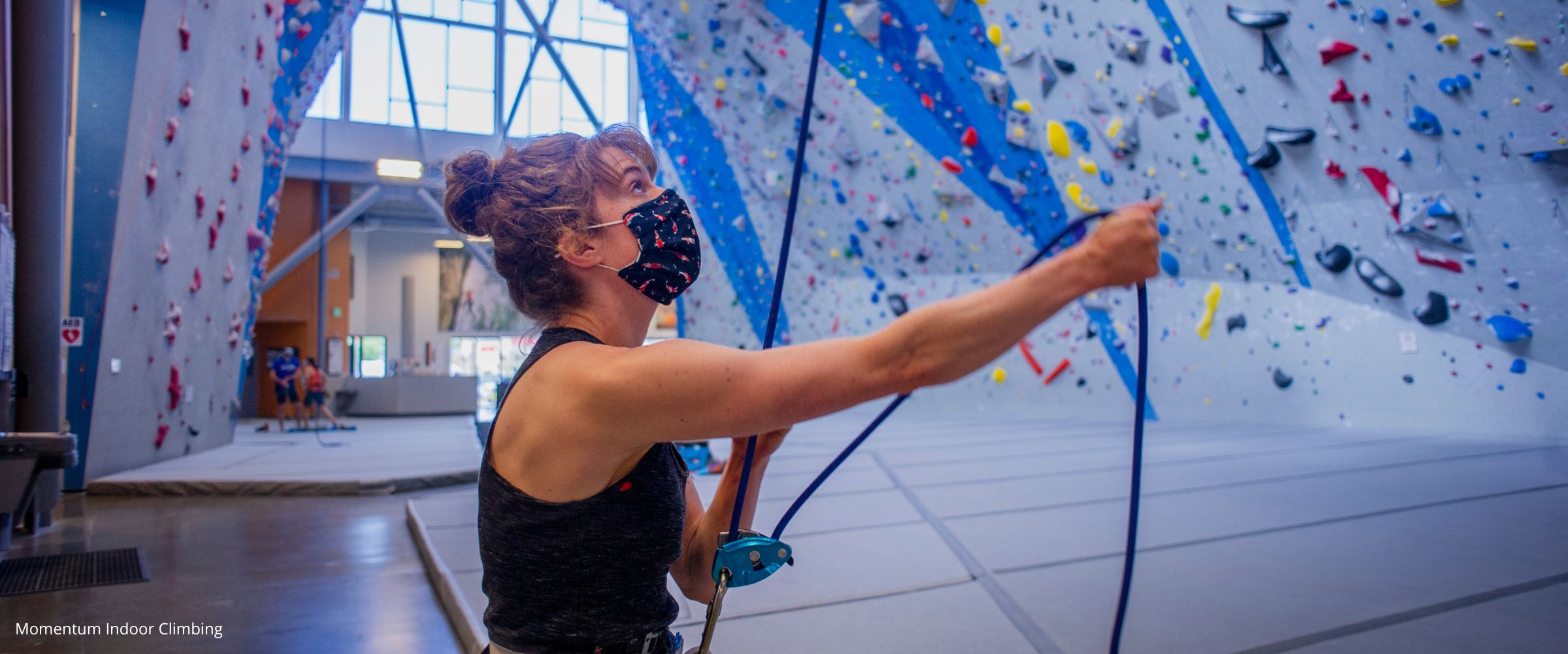 Person indoor rock climbing at indoor rock climbing gym using tubular belay device