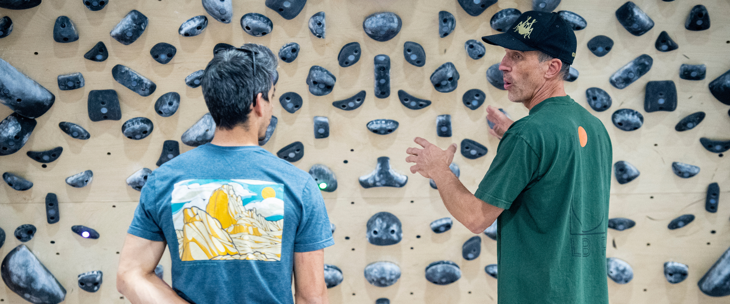 Indoor climbing gym staff talk in front of climbing wall