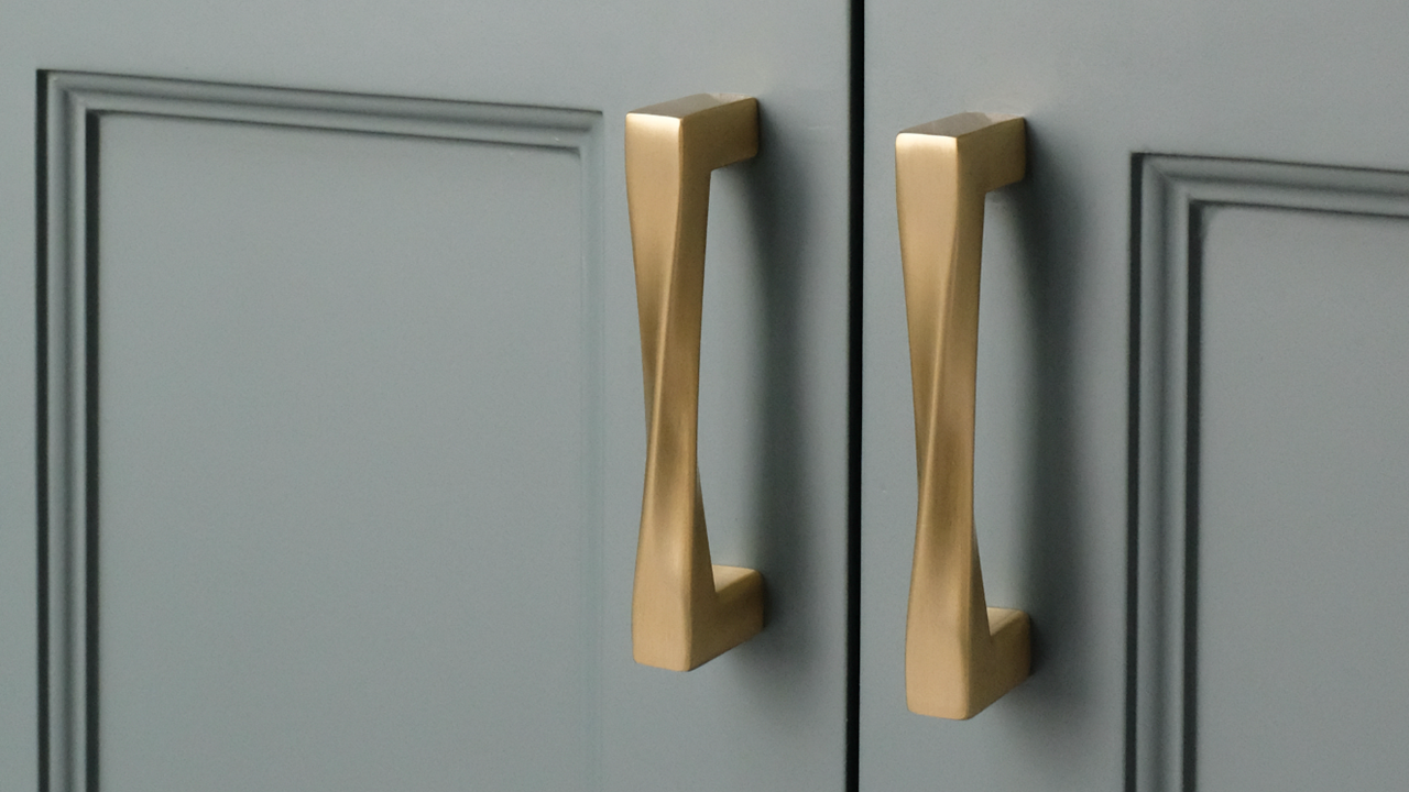 Two Hapny Twist Satin Brass pull handles on a blue bathroom cabinet