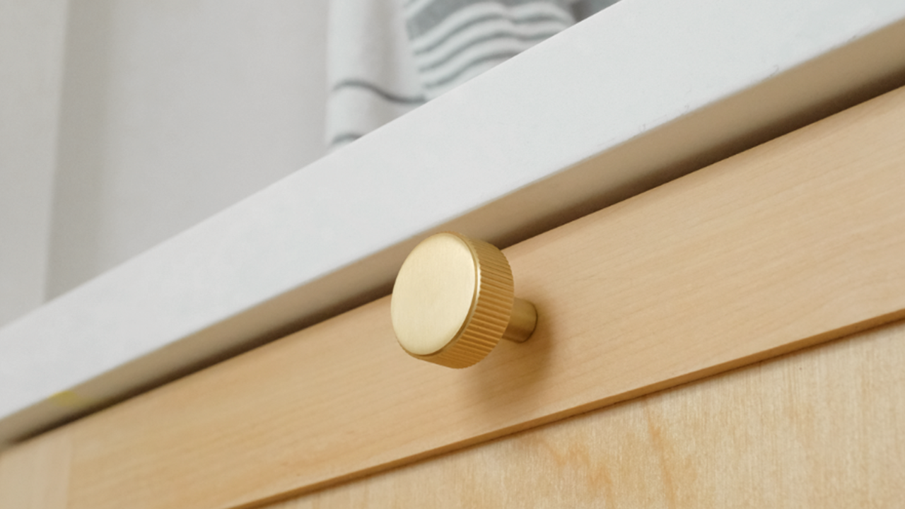 Hapny Ribbed Satin Brass knob installed on a wood bathroom drawer