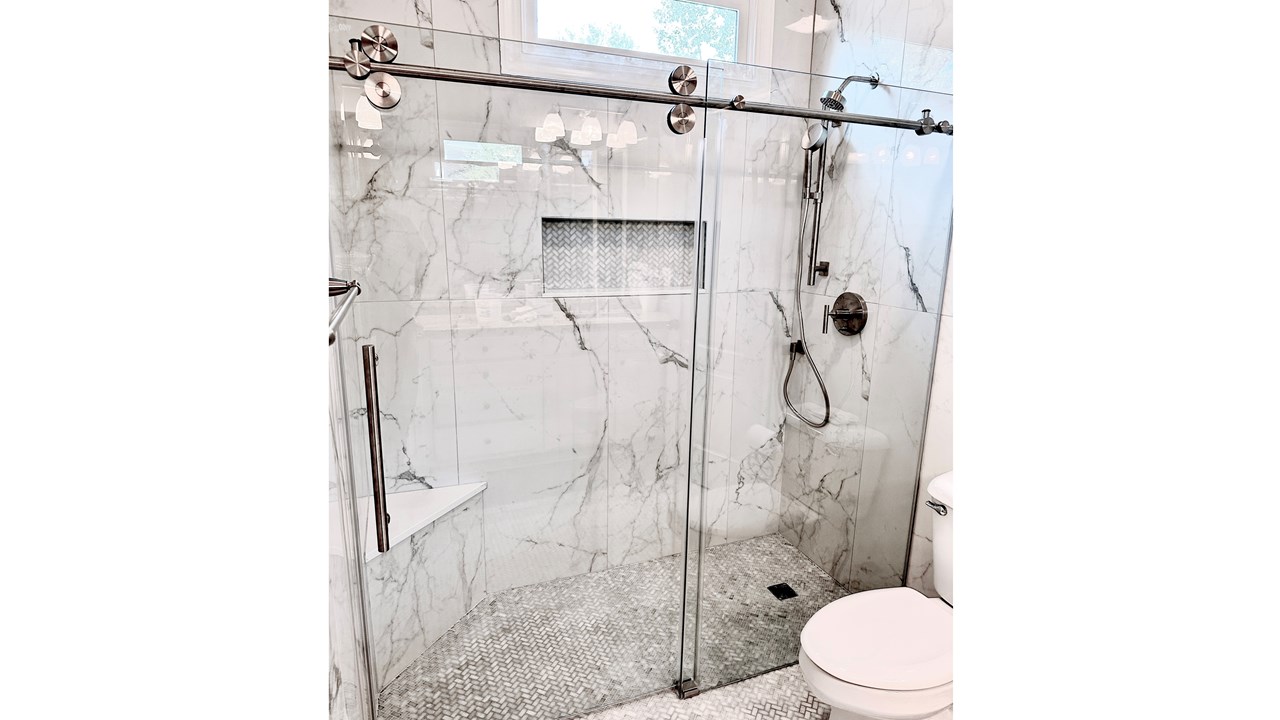 Modern curbless shower featuring large 24x48 wall tiles and a seamless frameless glass design
