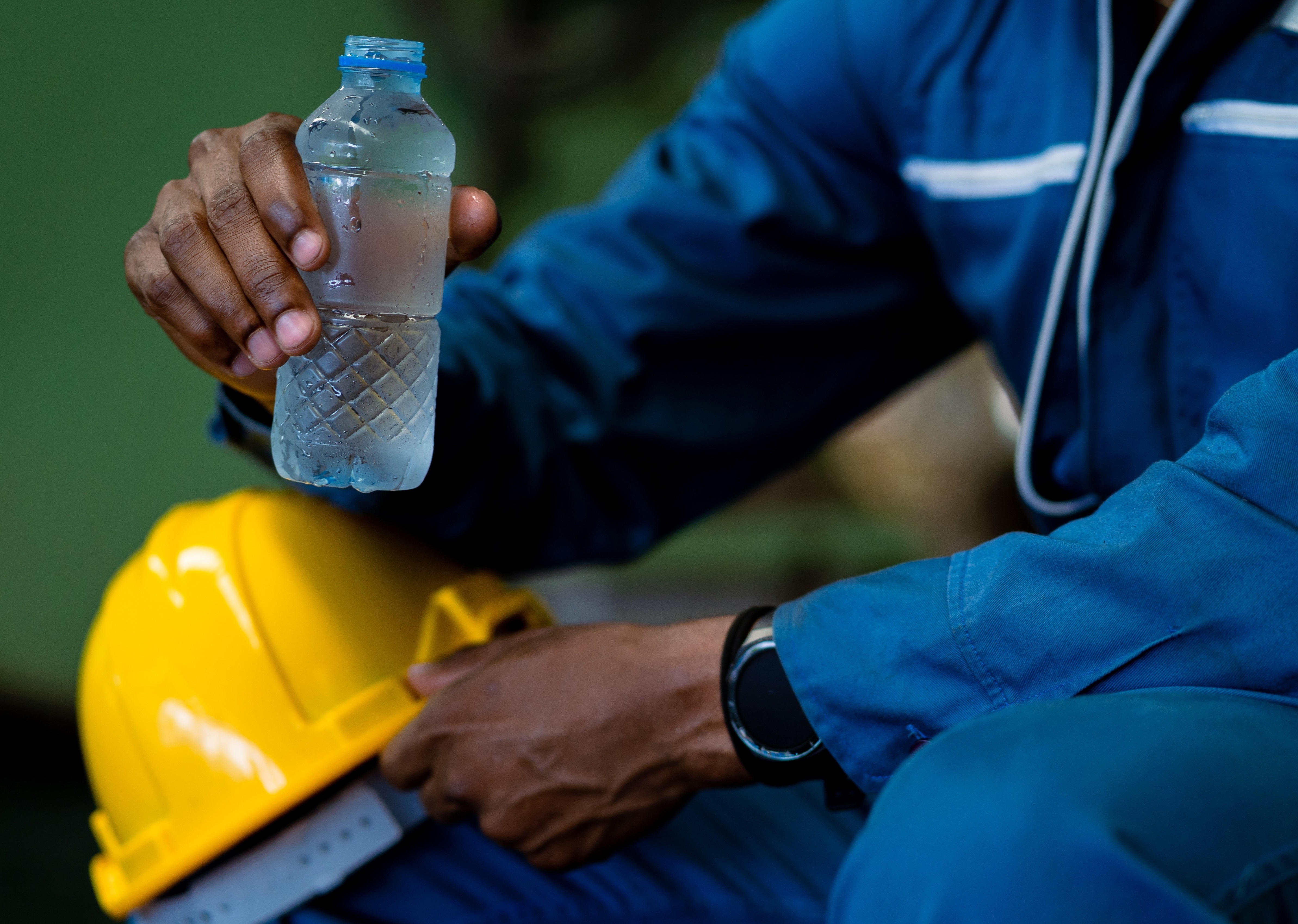 black male in work uniform holding cold bottle of water and yellow hard hat