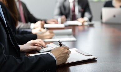 professionals in suits sitting around a meeting table and taking notes