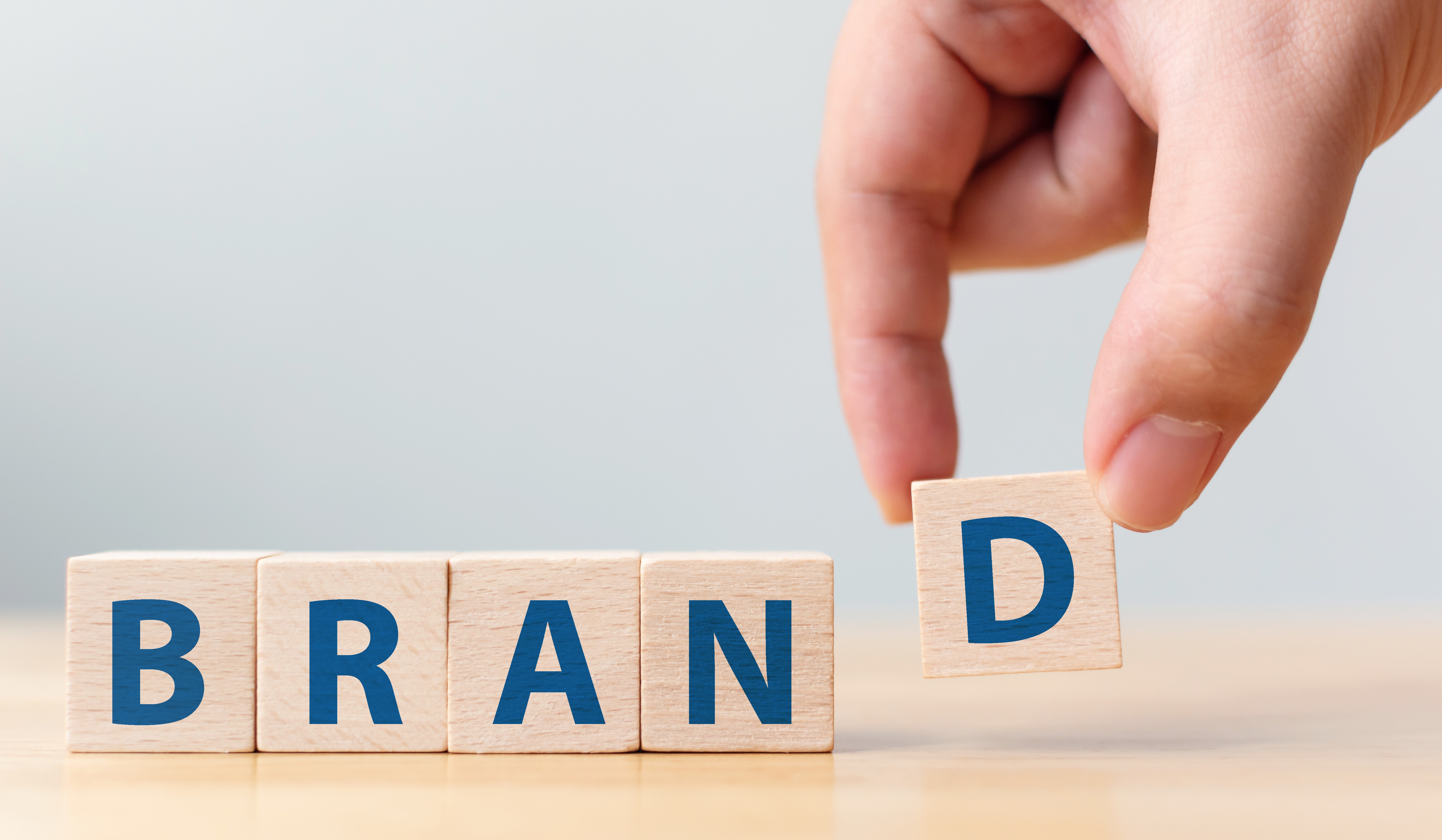 Hand of male putting wood cube block with word “BRAND” on wooden table. 