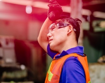 man wearing work vest, helmet and gloves wiping sweat from brow