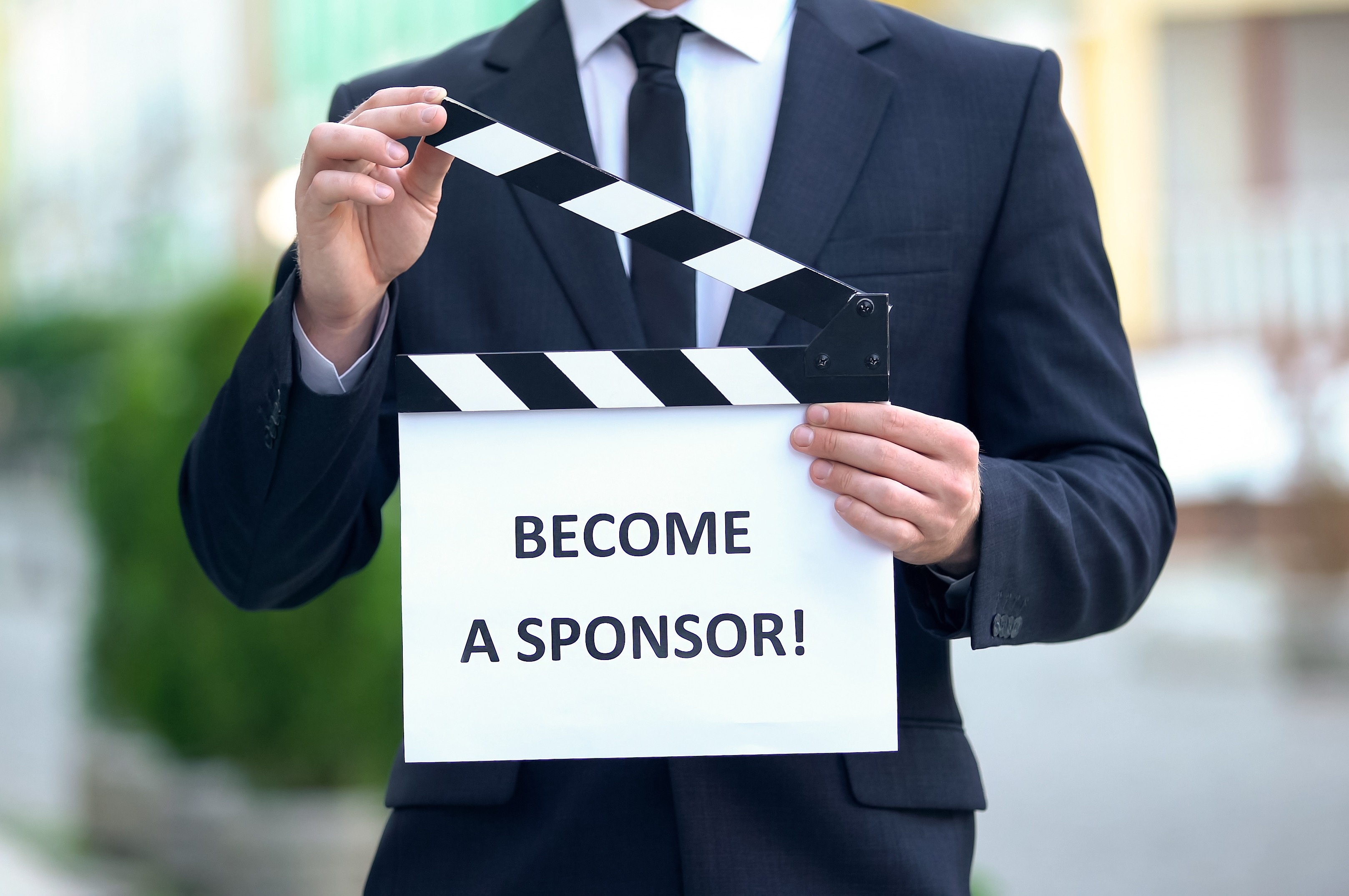 Man holding sign reading Become a Sponsor