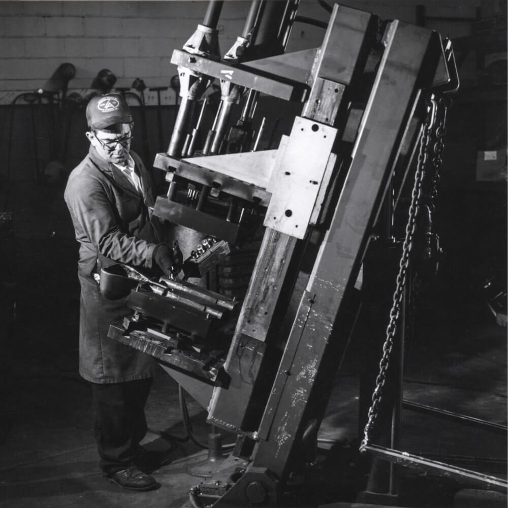 Historical black-and-white photograph of a worker beside manufacturing equipment