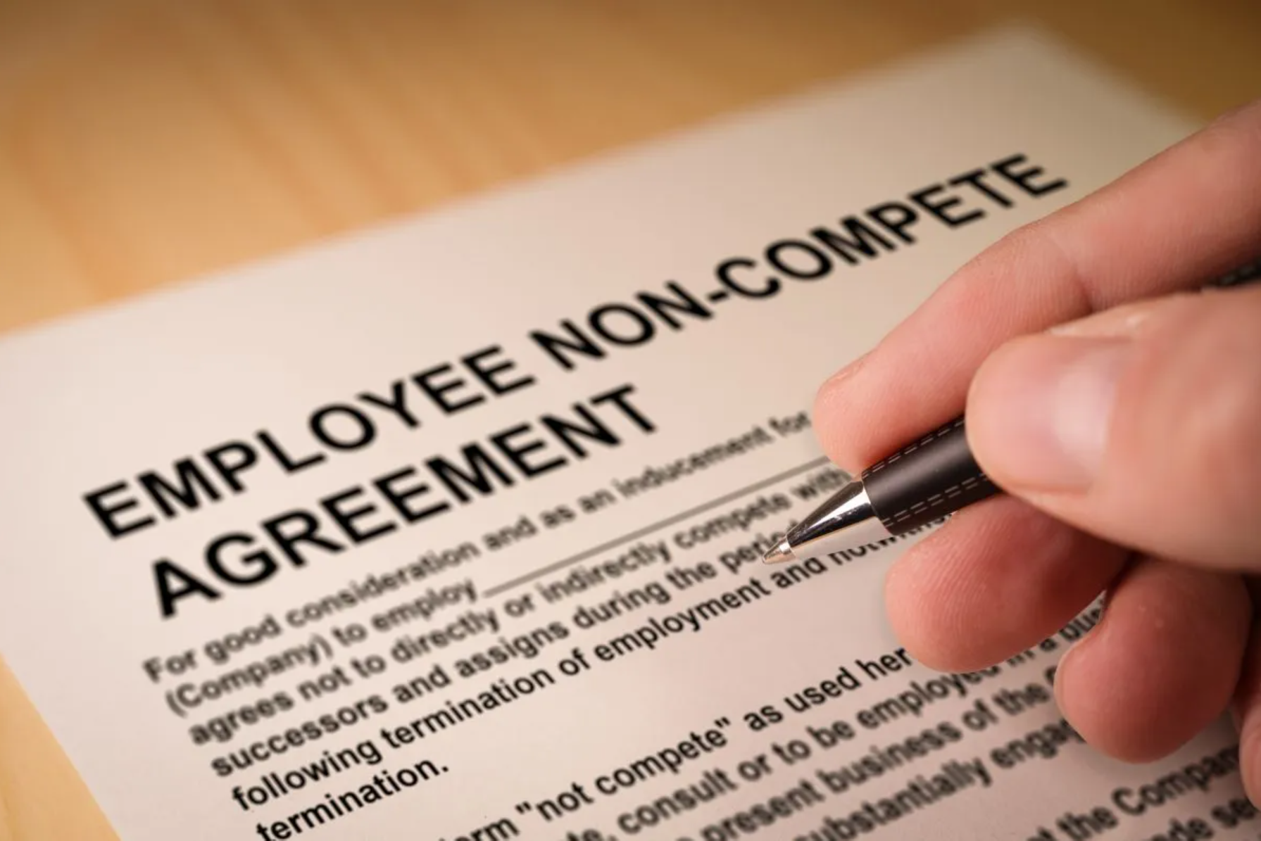 Hand holding pen over paper reading "Employee Non-Compete Agreement"