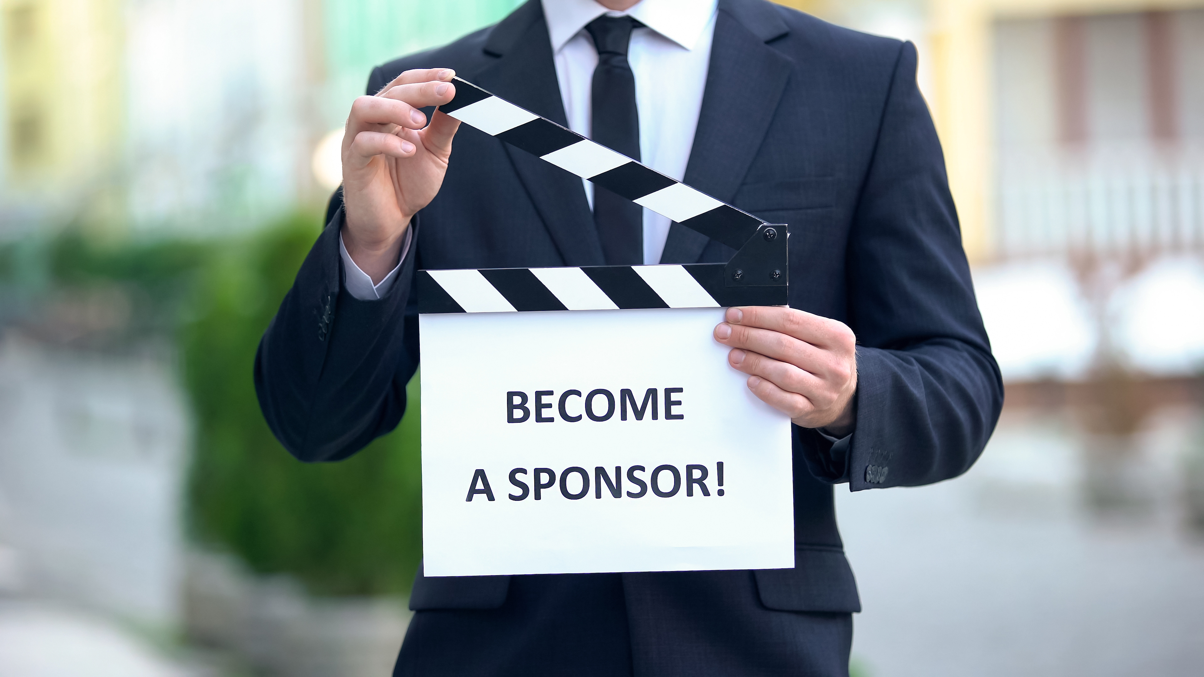 Man holding sign reading Become a Sponsor