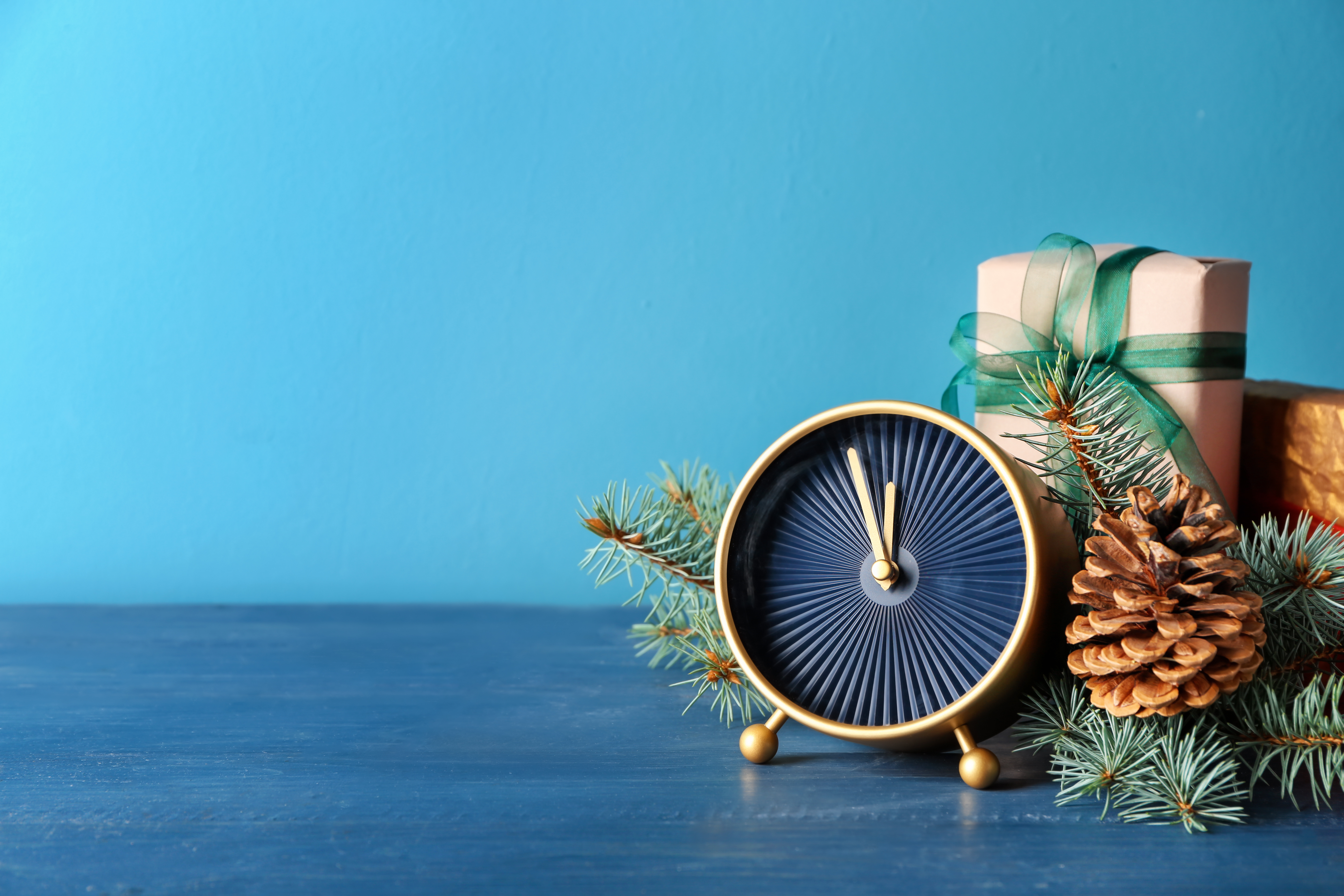 a small black and gold clock next to pine needs, a pine cone, and wrapped gifts