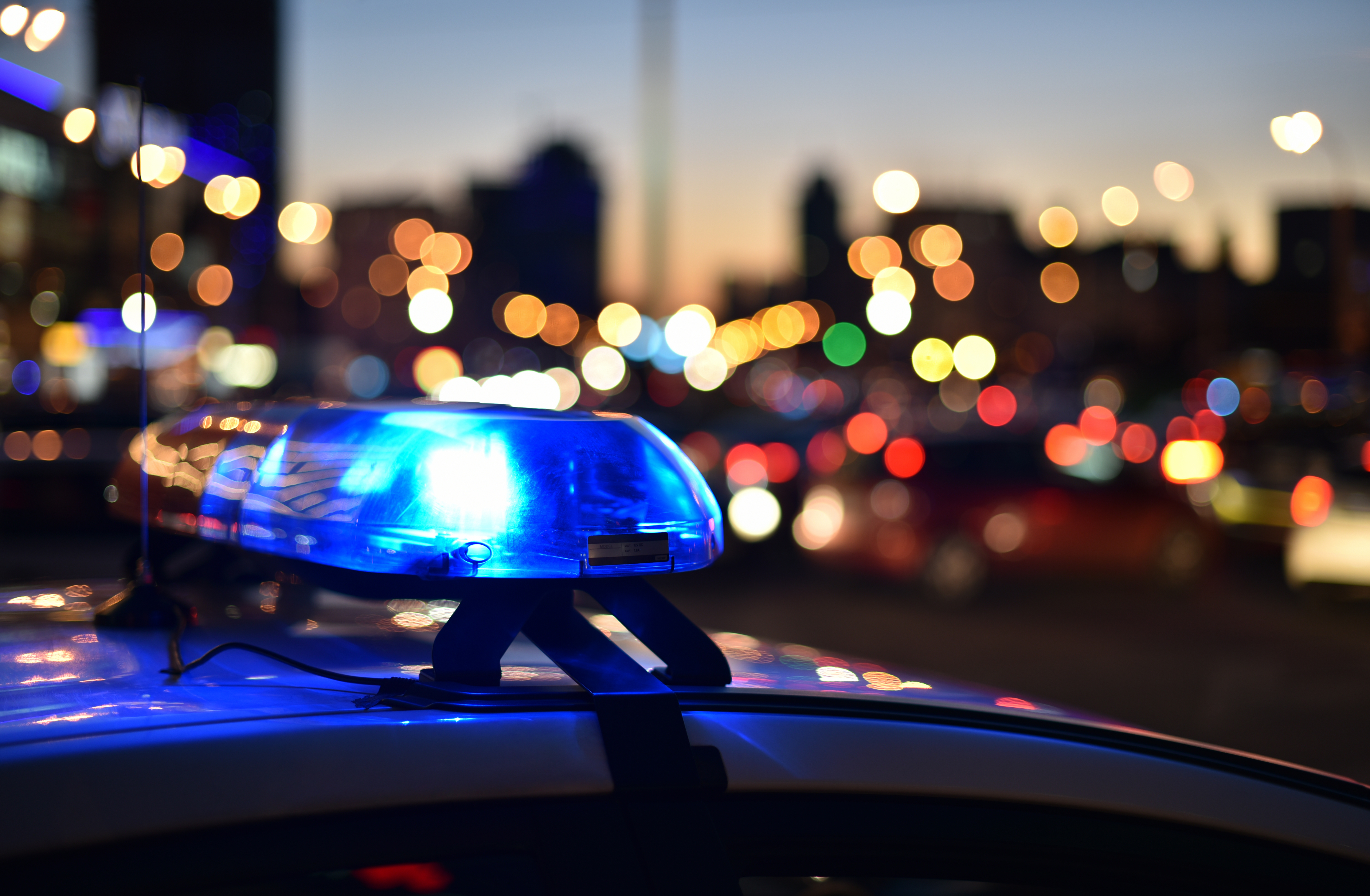 a police car with lights lit in front of a busy street.