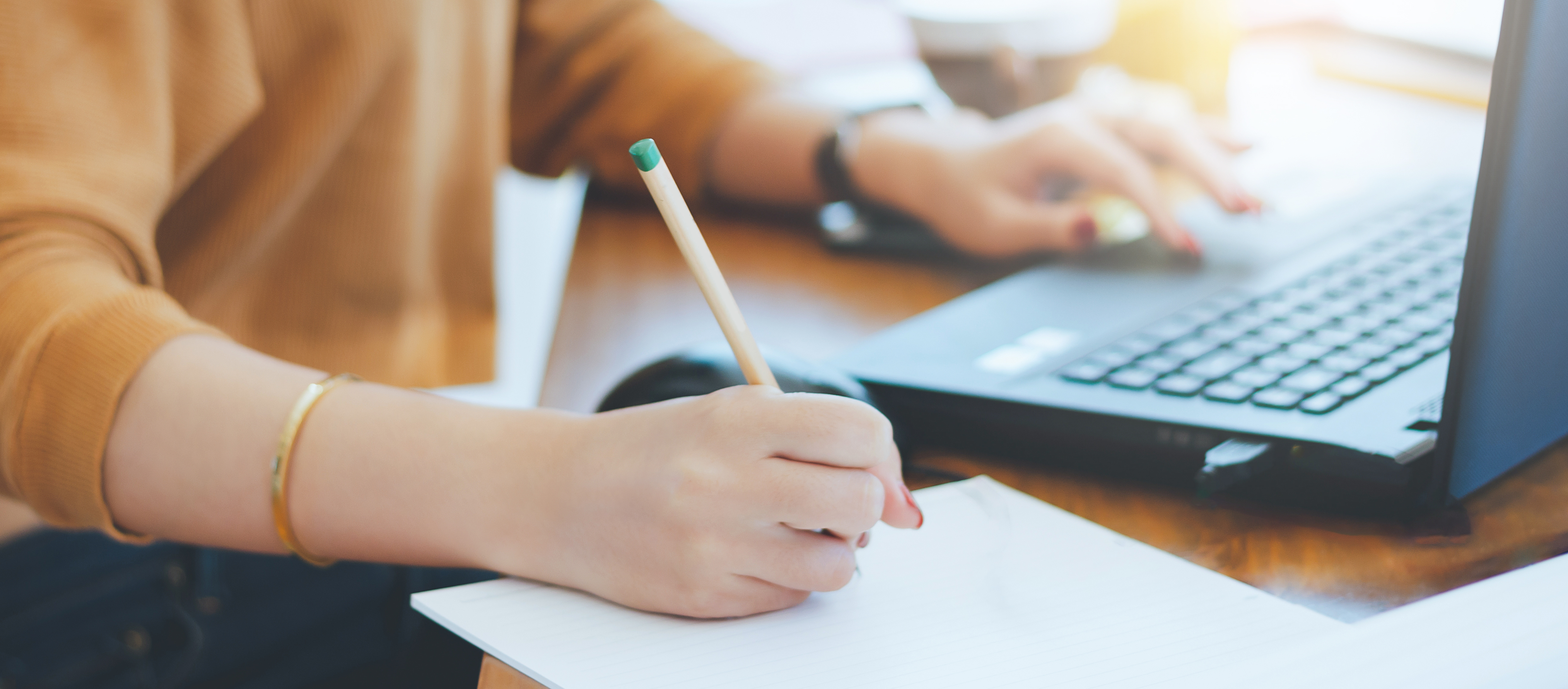 a therapist takes notes on piece of paper while looking at a laptop.