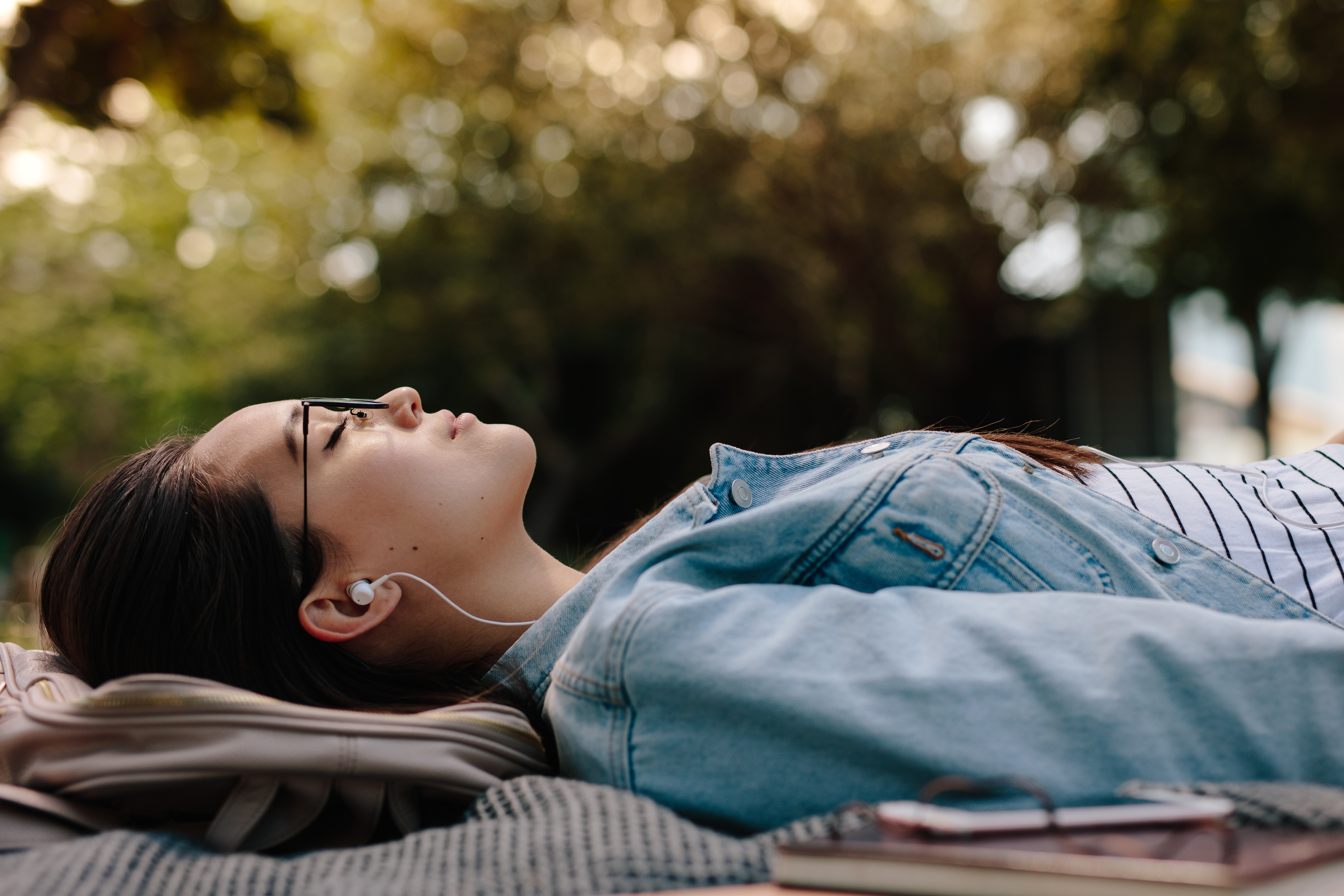 a therapist lays on a blanket on the ground next to a book, wearing earbuds.