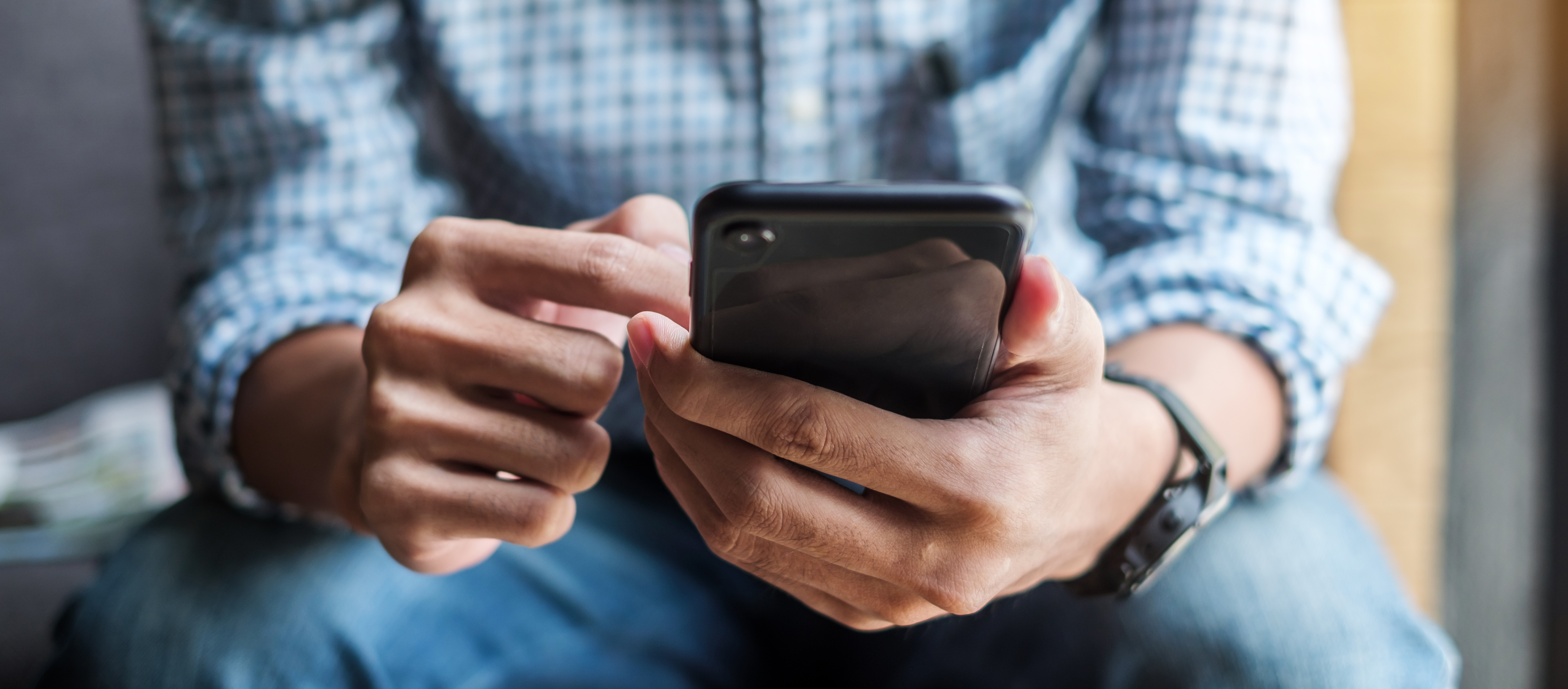 A therapist in a blue plaid shirt and jeans scrolls on a smart phone