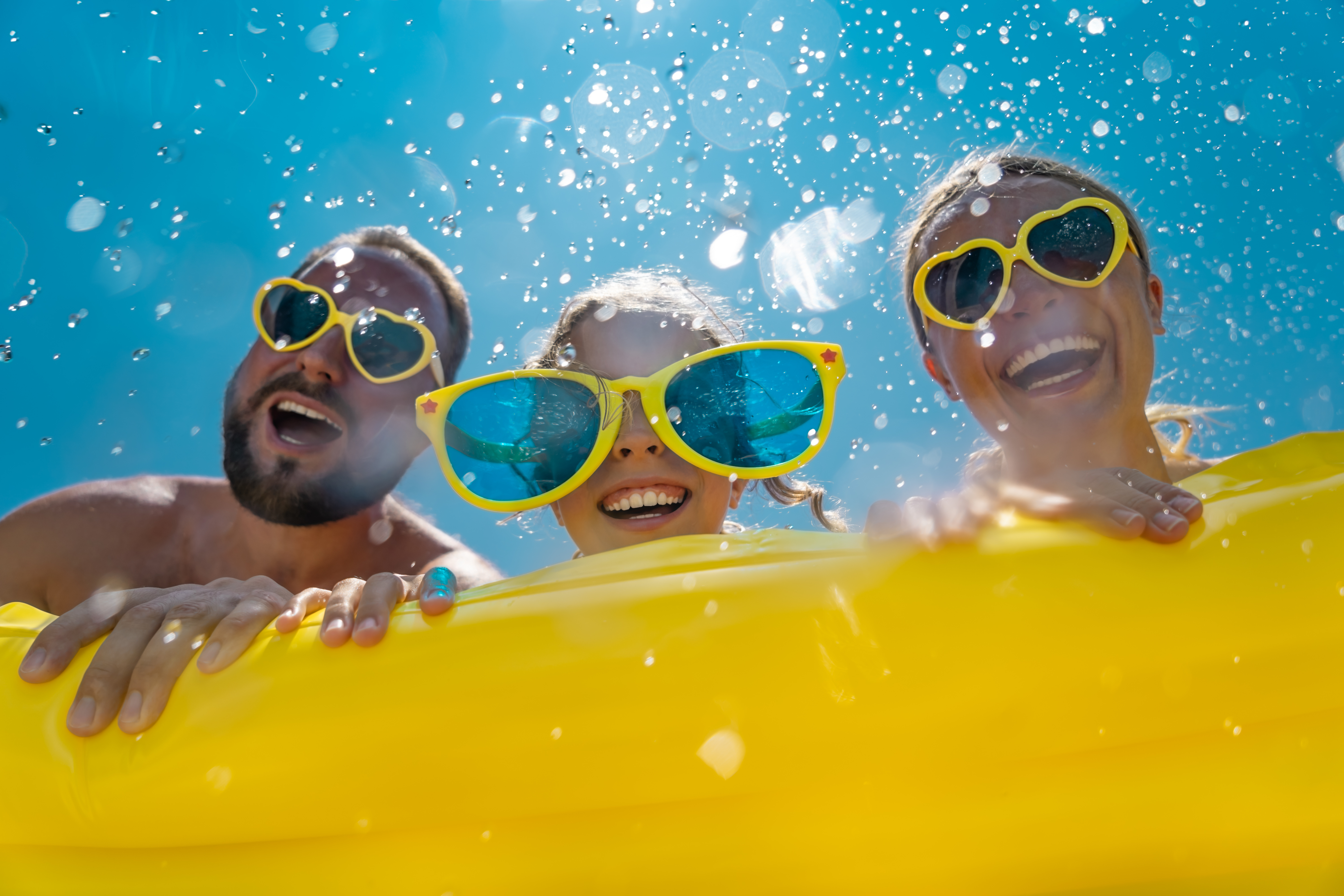 a mother, a father, and a daughter, each wearing sunglasses while laying on a yellow raft