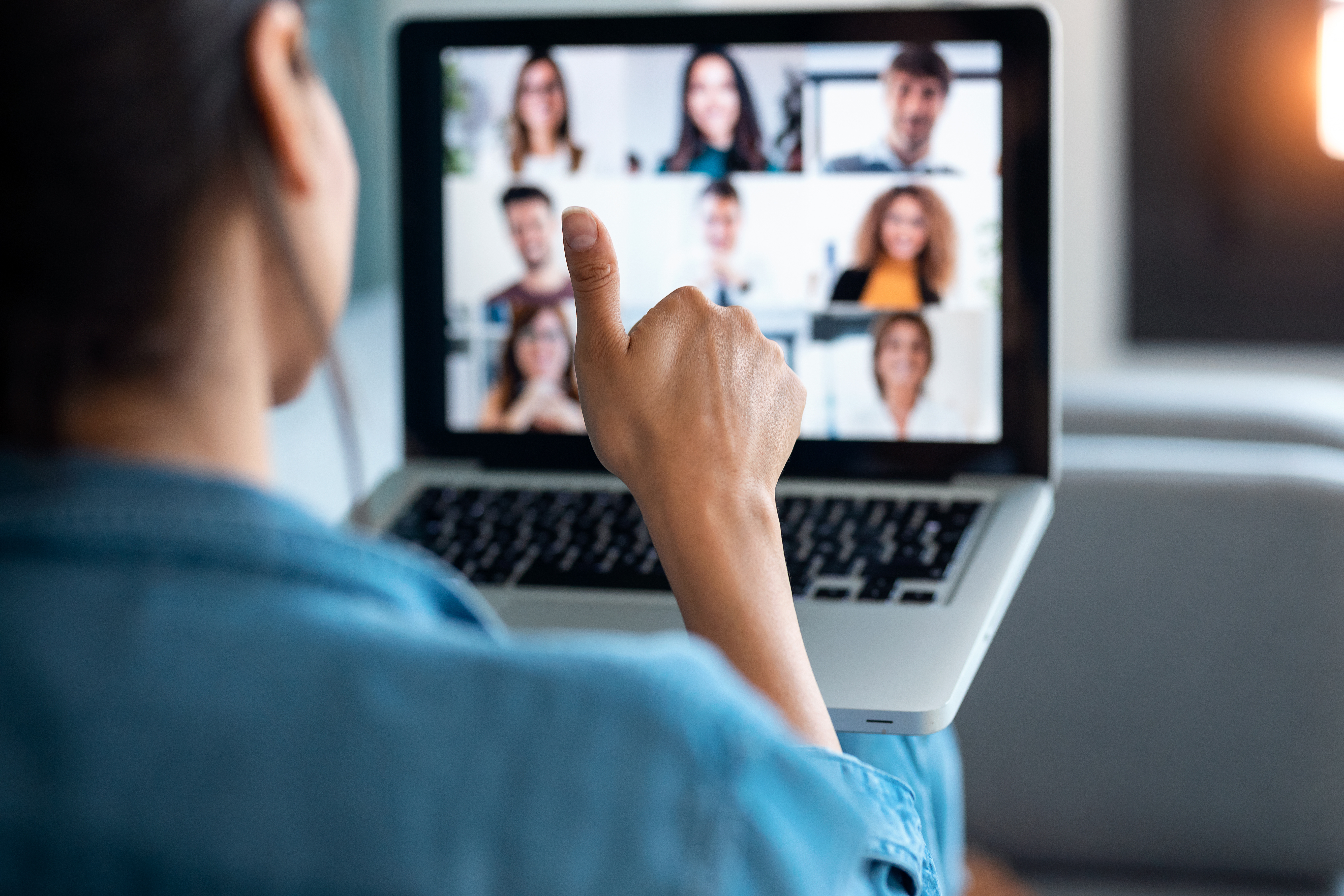 a therapist sits in front of a computer and gives a thumbs up to a group of clinicians on a call