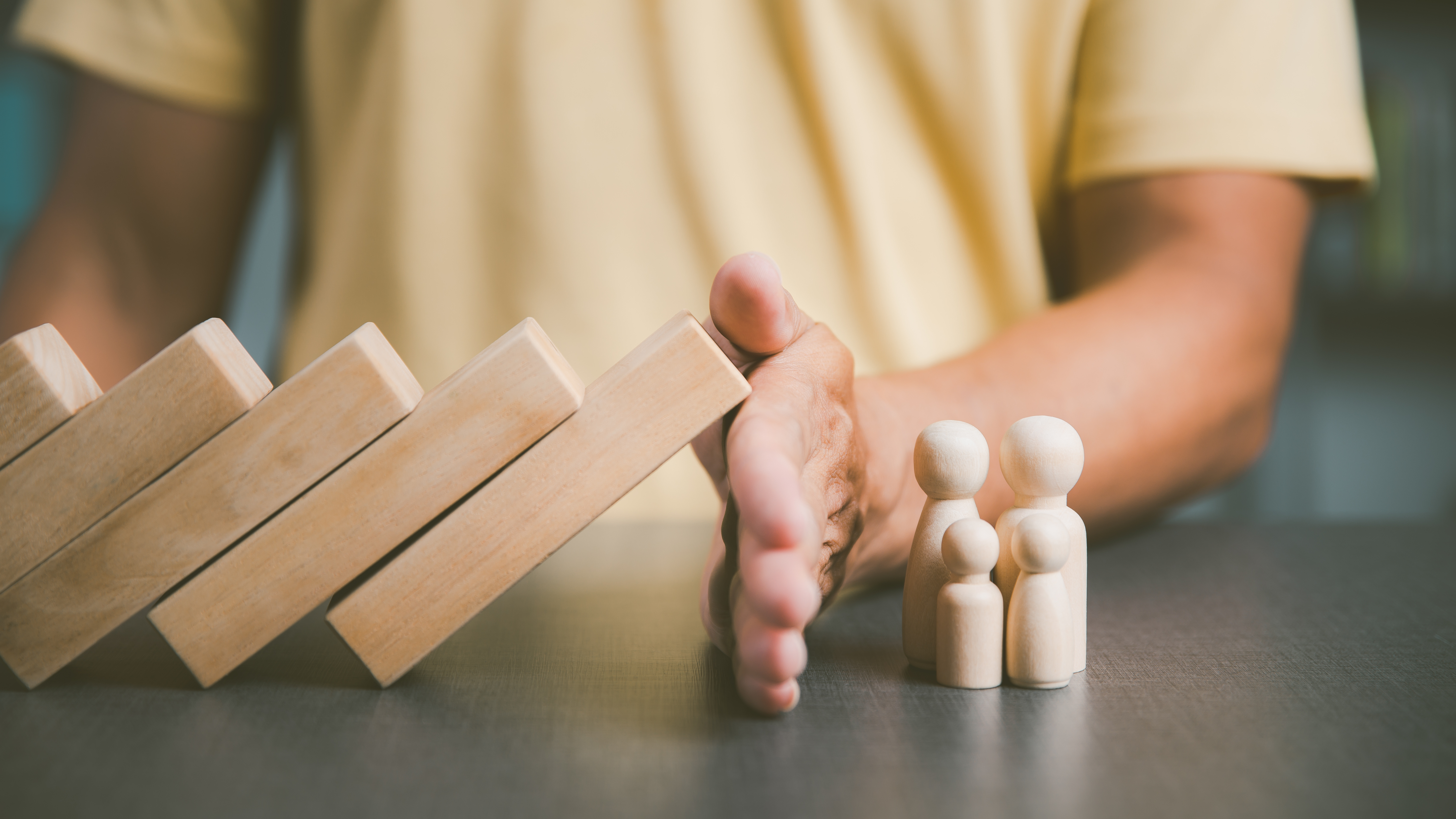 a hand keeps a set of blocks from falling on four wooden figures.