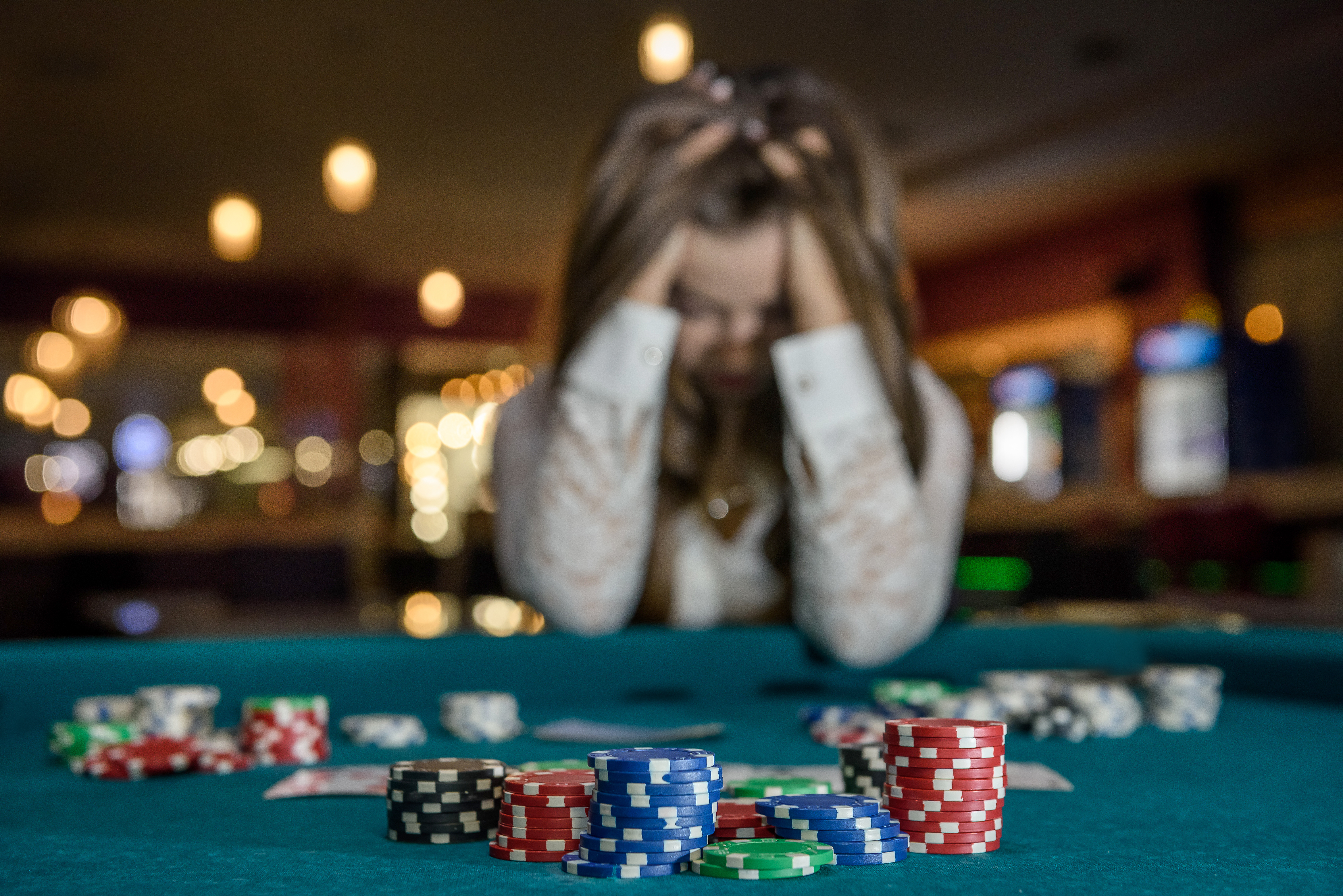 a woman sitting at a casino table lined with poker chips, holding her head in her hands.