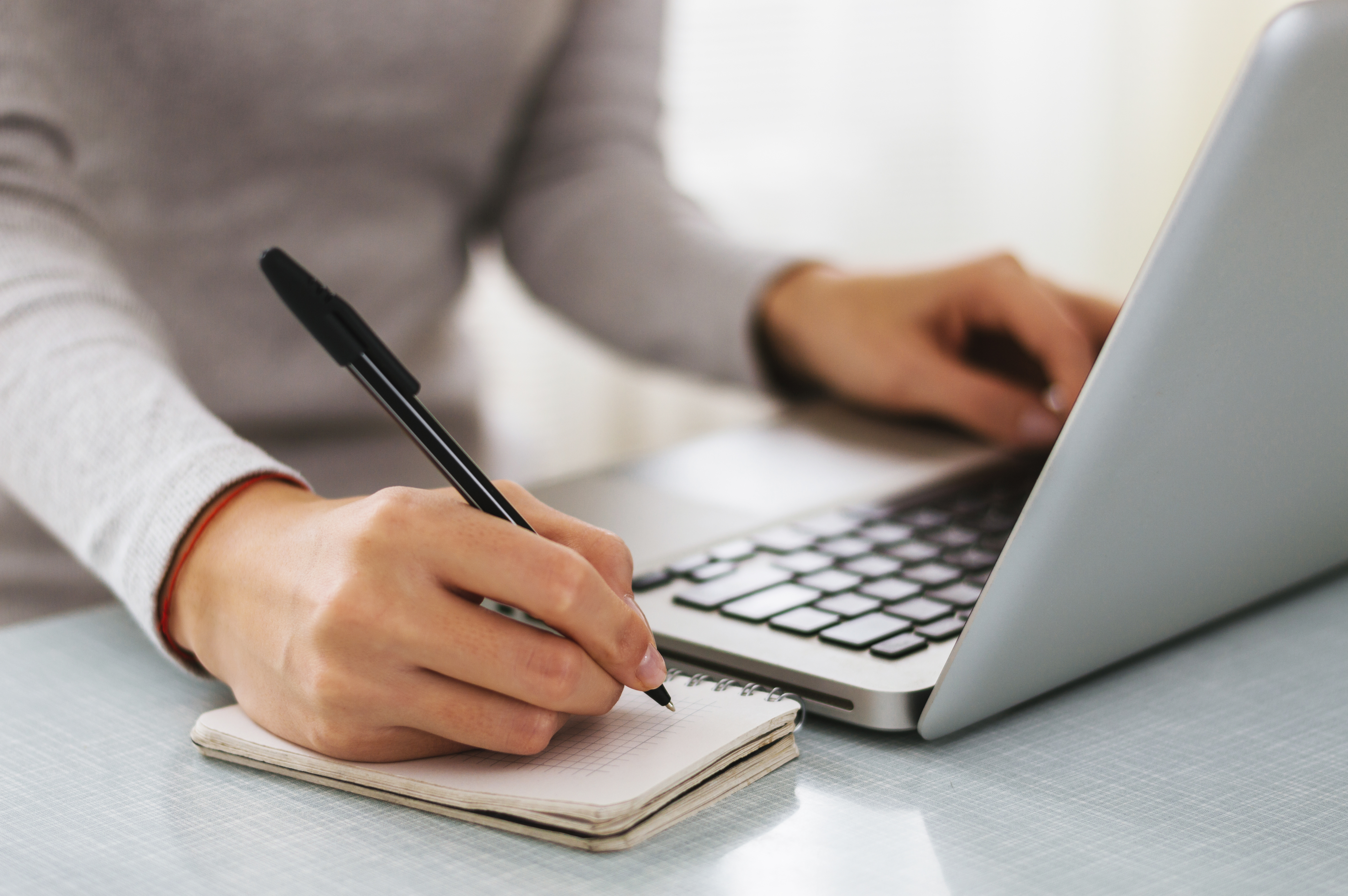 A therapist sits in front of an open laptop and takes notes on a small notepad