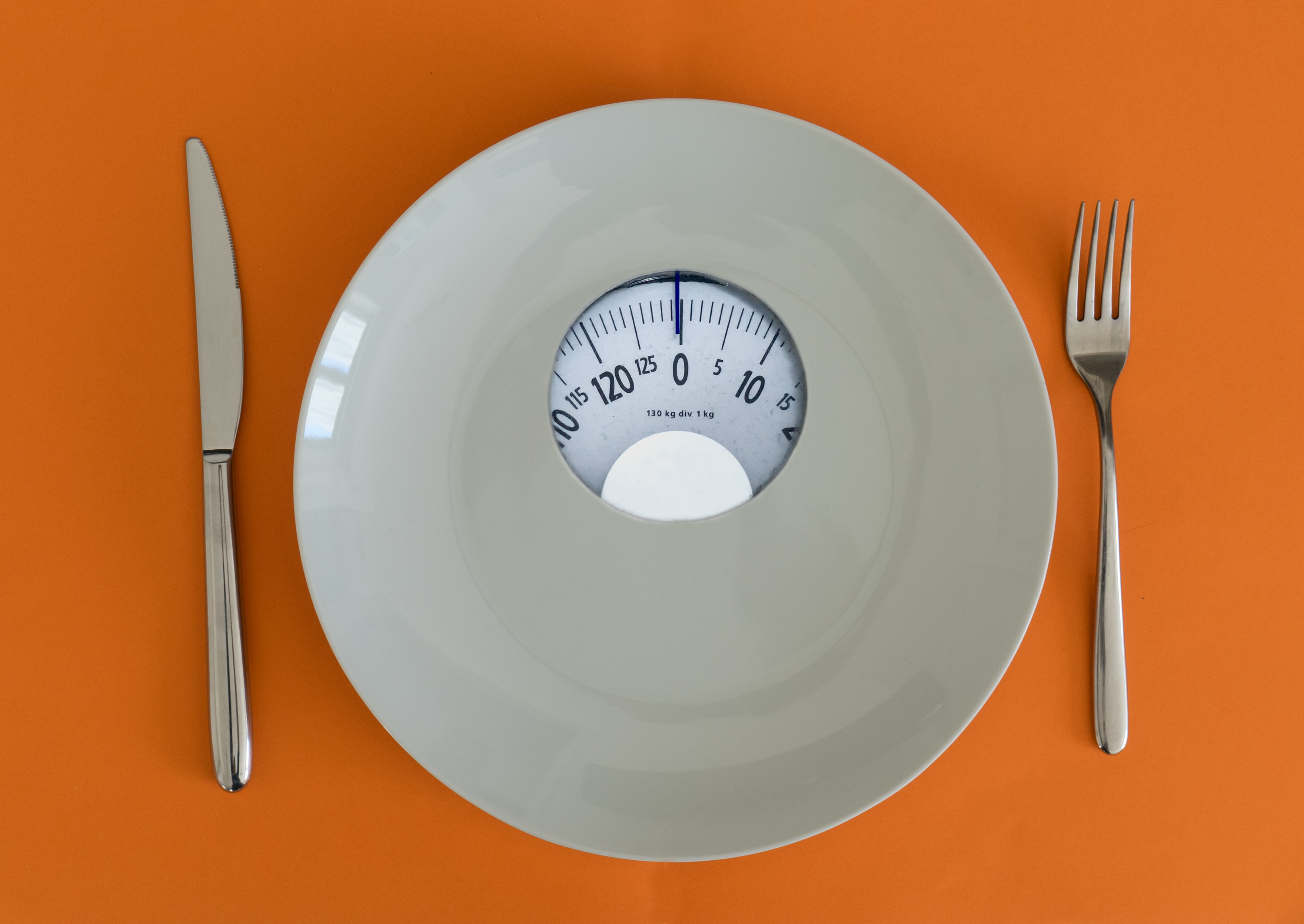 a fork and knife set next to a scale on an orange background.