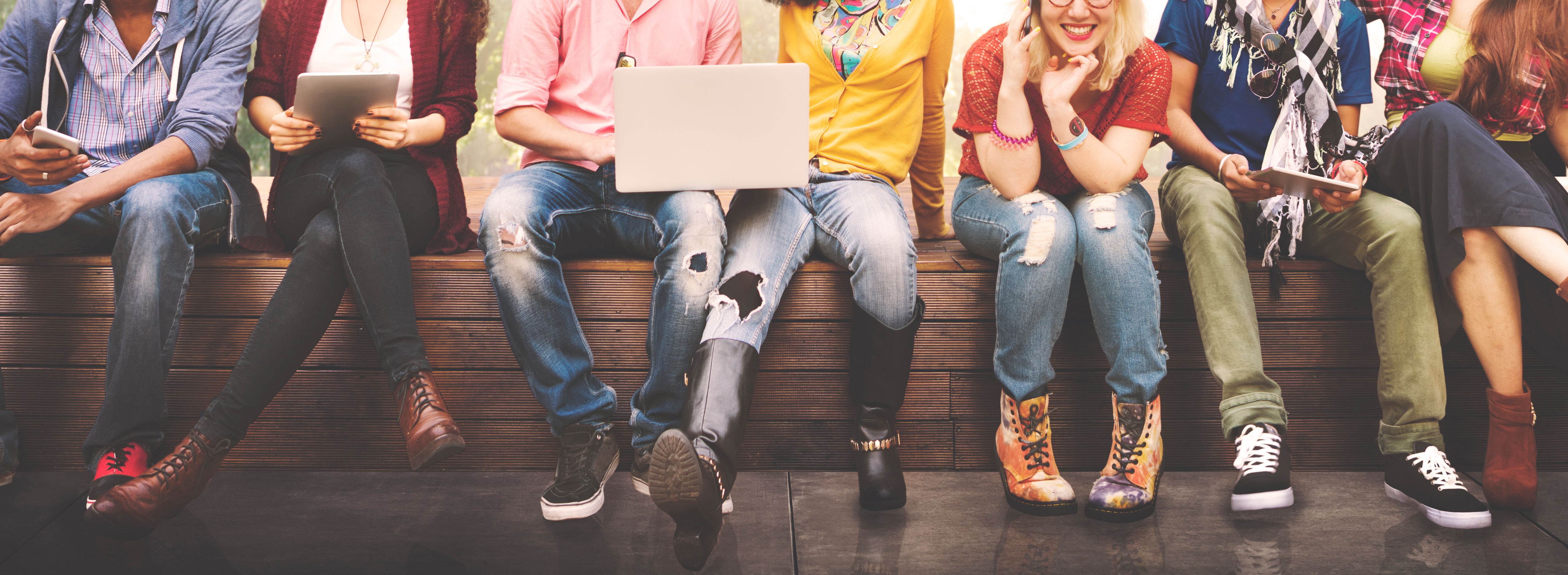 A group of young people sit together on a bench. 