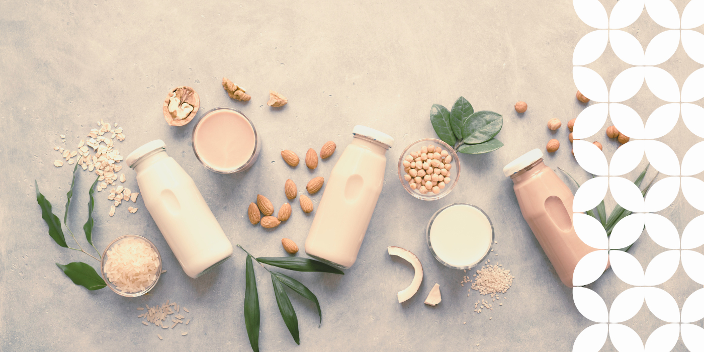 Assorted plant-based milk bottles are surrounded by ingredients like almonds, oats, and soybeans on a textured surface, creating a natural and fresh vibe.