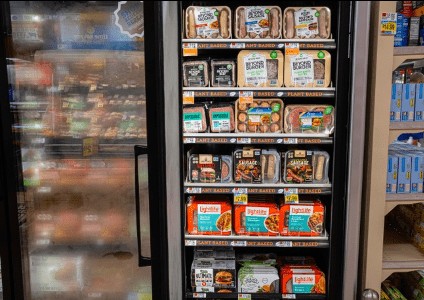 An open retail refrigerator case stocked with various packaged plant-based meats from brands like Beyond Meat and Lightlife, organized across shelves labeled "PLANT BASED".