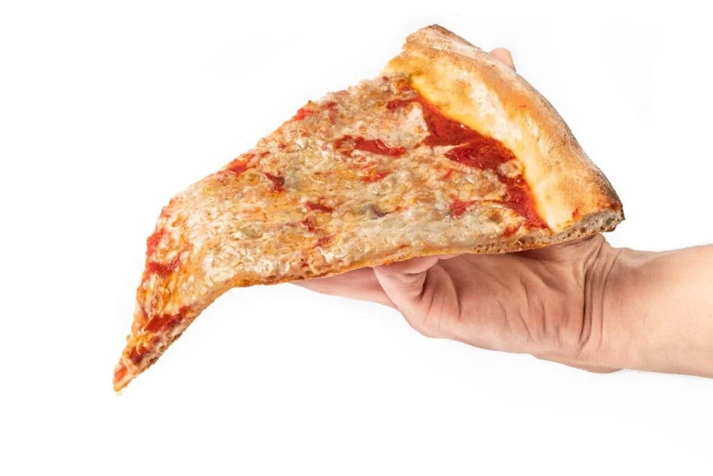 A side profile shot of a person's hand holding a single large slice of plain cheese pizza with a thick, golden-brown crust against a solid white background.