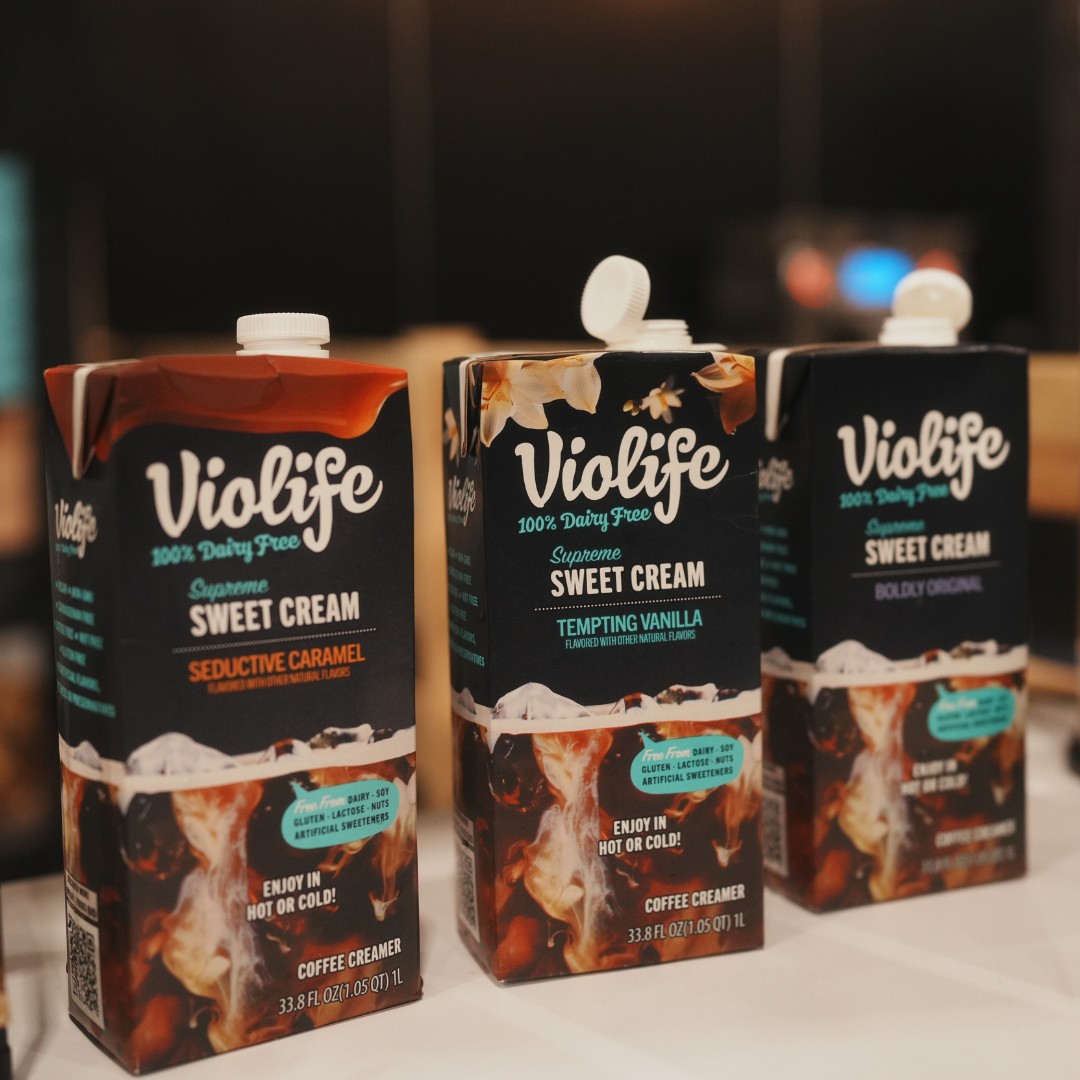 Three 1-liter cartons of Violife 100% Dairy Free Supreme Sweet Cream coffee creamer lined up on a table. The caramel flavor is on the left, vanilla is in the center, and the original flavor is on the right.
