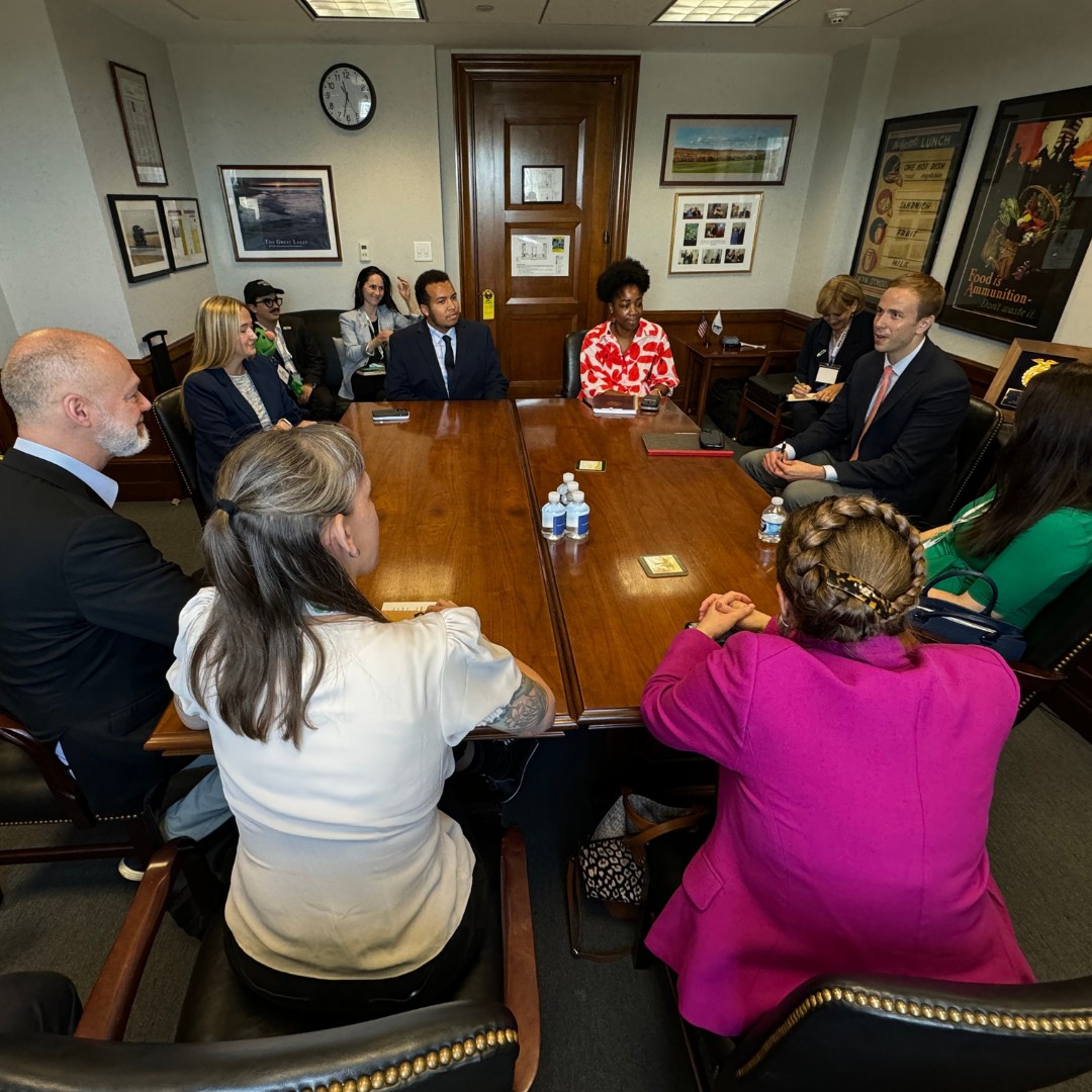 A high-angle view of an interactive meeting where a diverse group of professionals in business attire are seated around a double-segment wooden conference table inside an office room.