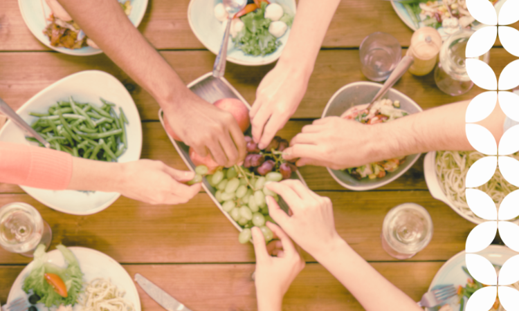 Hands reaching for food in the center of a table, indicating people coming together in community
