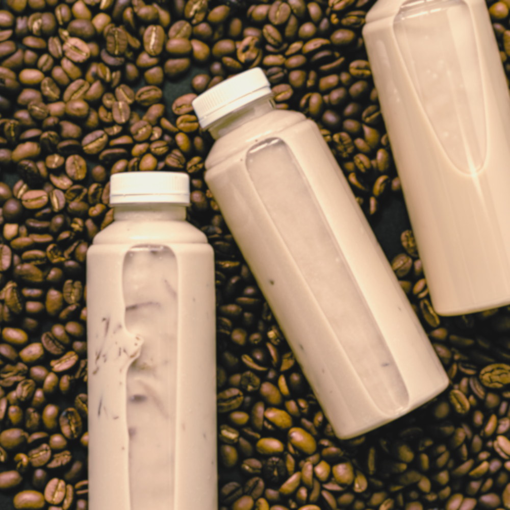 Bottled plant-based coffee beverages laying in a pile of coffee beans.