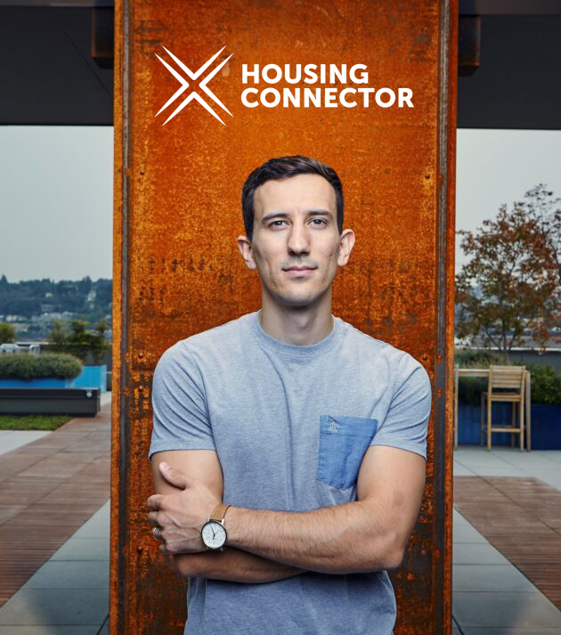 A man with his arms crossed in front of a sign that says housing connector