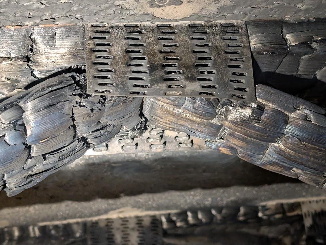 Close-up of a charred metal connector plate at a truss joint