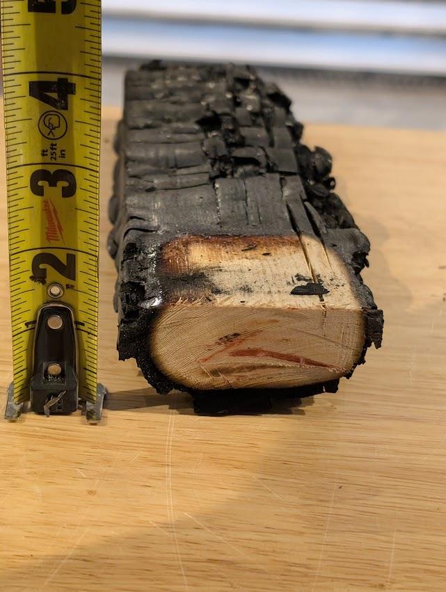 Charred chord member section next to a tape measure showing remaining sound wood
